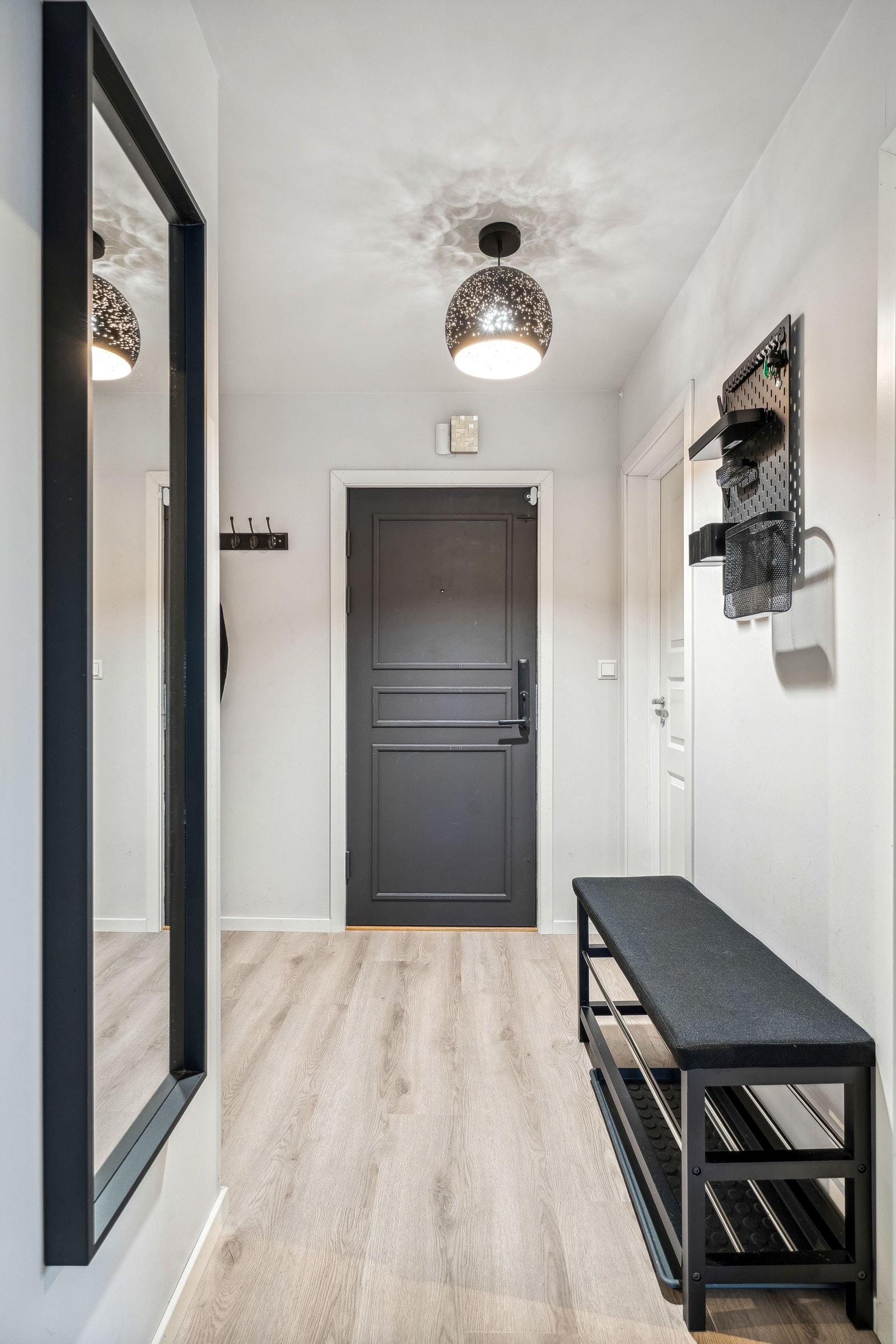 Stilig gang med malt svart inngangsdør og praktiske, innfelte oppbevaringshyller som gir både funksjonalitet og et moderne uttrykk. Galleribilde
