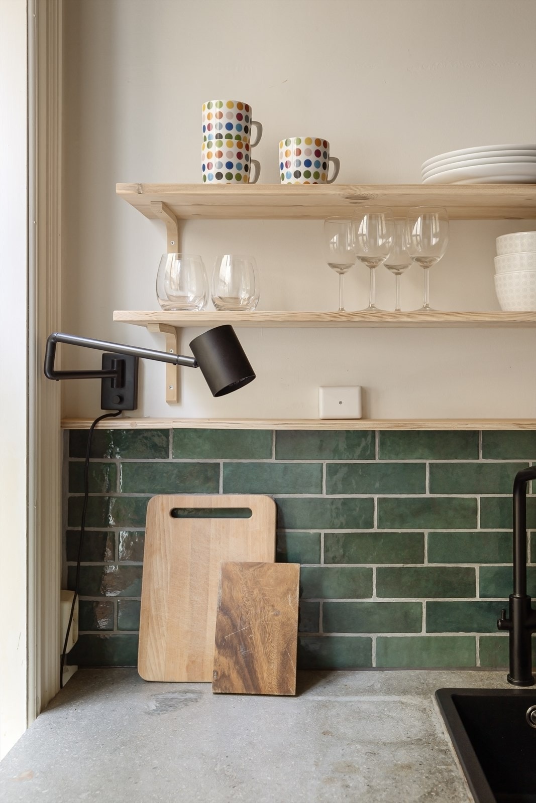 Kjøkkenet har sorte detaljer og lekre, grønne fliser Galleribilde