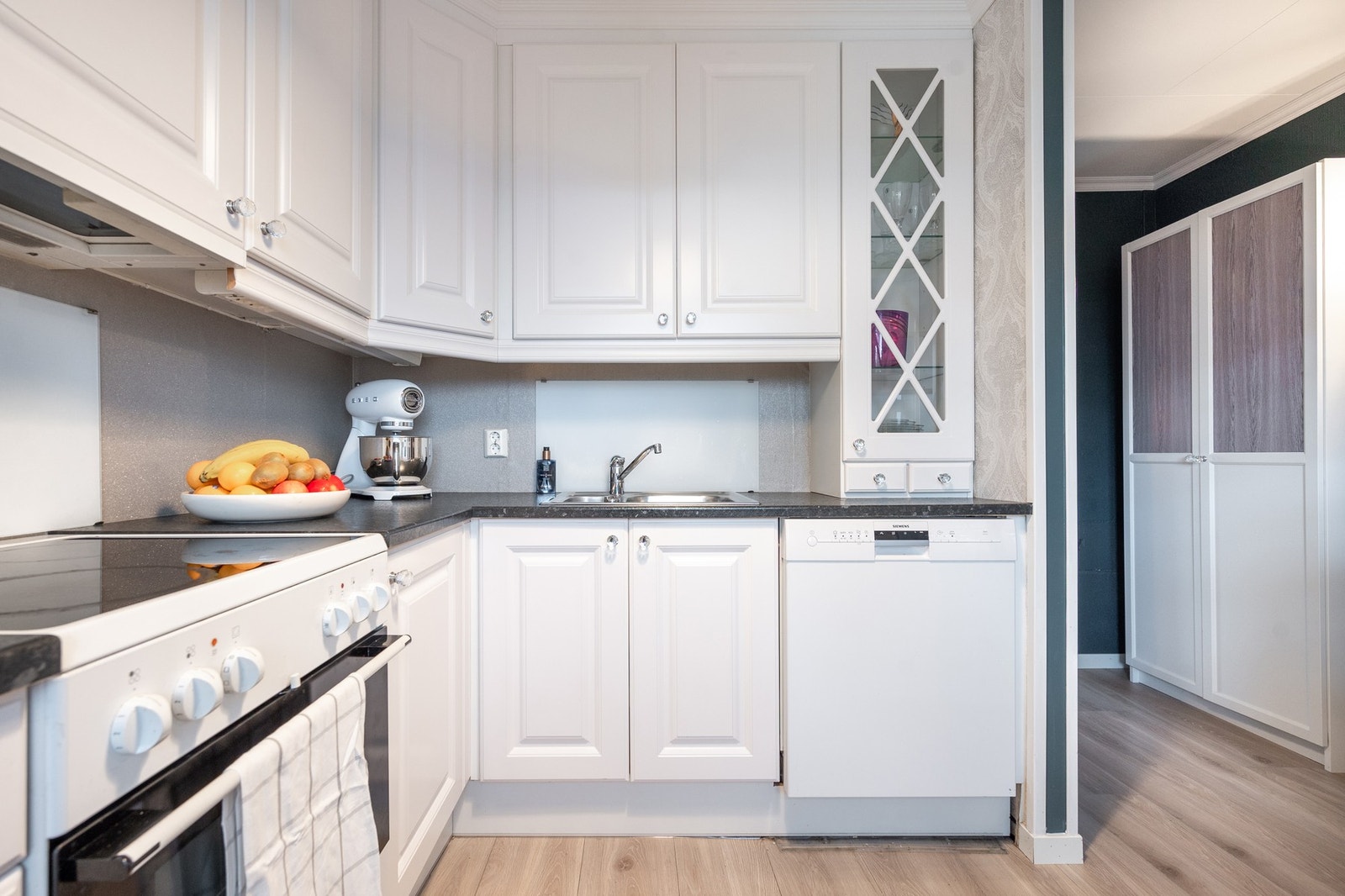 Vinkelformet kjøkkeninnredning fra JKE design med lyse profilerte fronter og sort laminerte benkeplater. Galleribilde