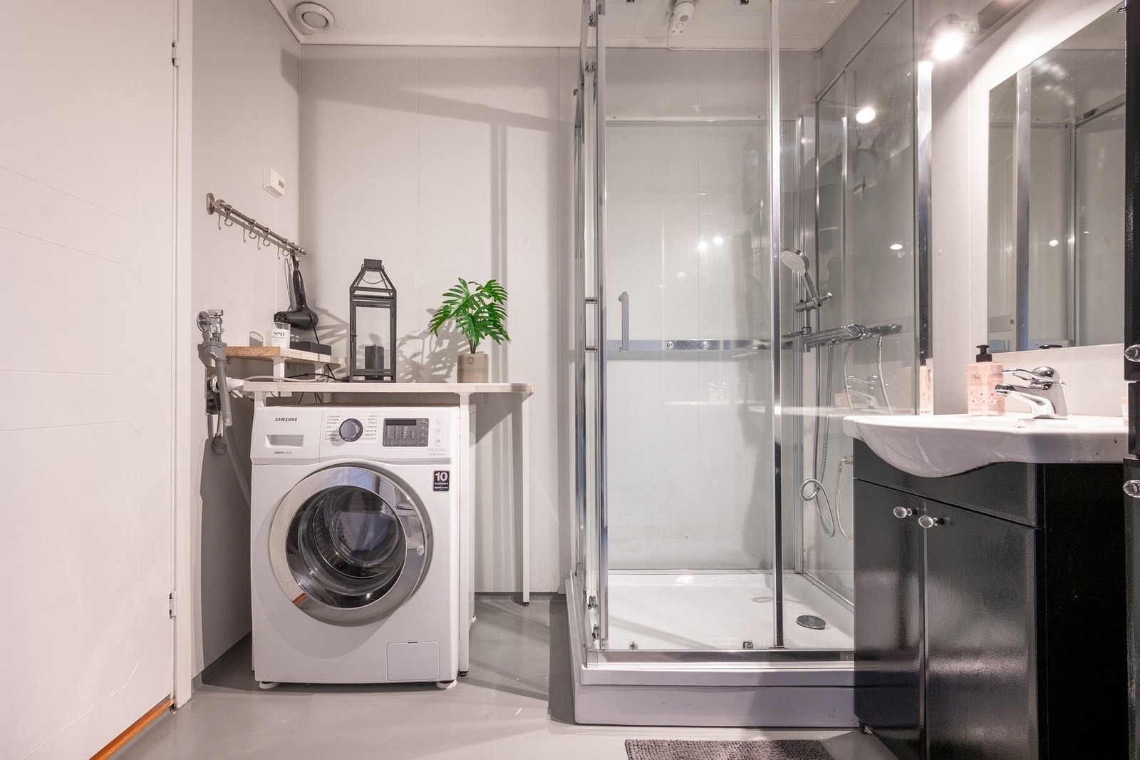 Lyst bad med servantinnredning med speil og belysning, dusjkabinett, toalett og opplegg for vaskemaskin. Galleribilde