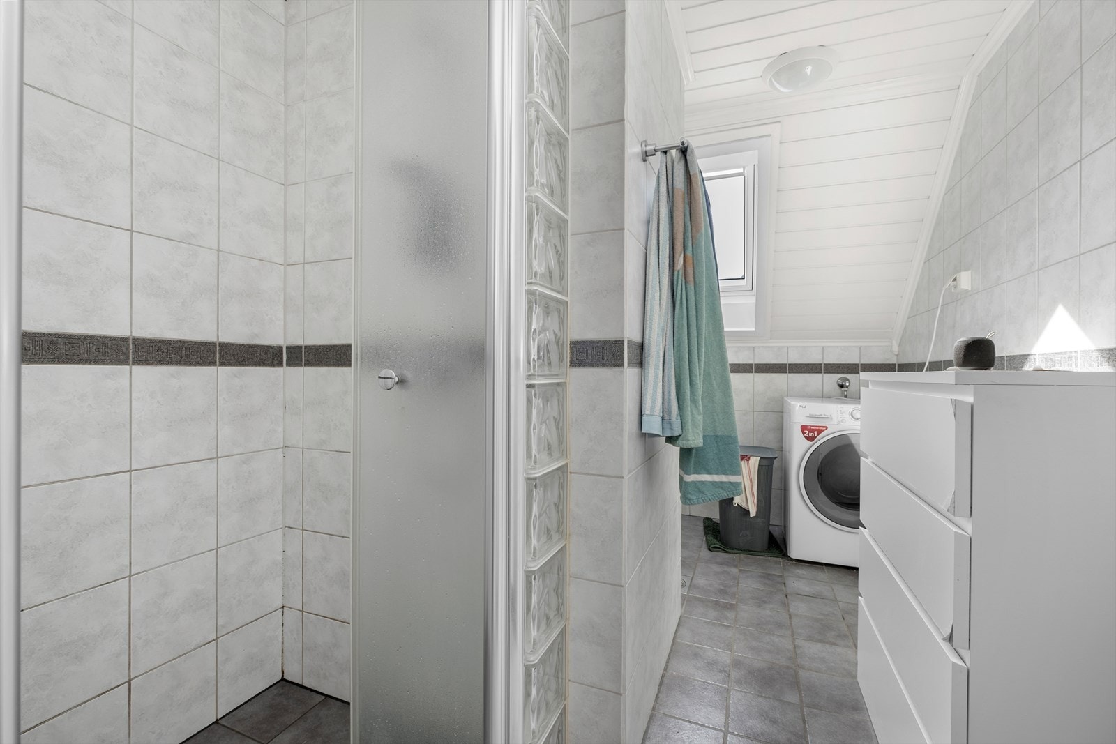 Badet er utstyrt med dusjhjørne, servant med underskap og opplegg for vaskemaskin. Galleribilde