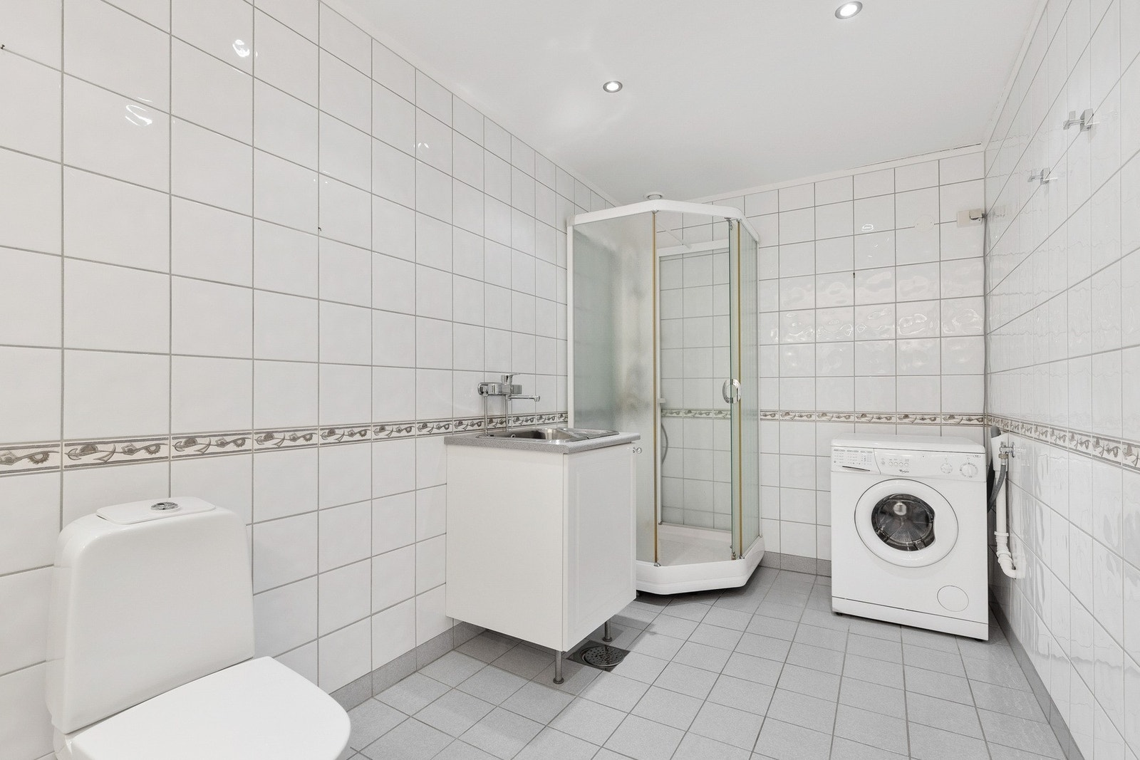 Badet er utstyrt med gulvstående toalett, dusjkabinett, servantinnredning og opplegg til vaskemaskin Galleribilde