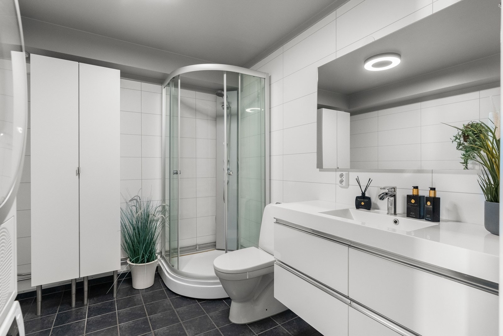 Bad med fliser på gulv og baderomsplater på vegger. Innredningen består av et underskap, servant, speil og ett dusjkabinett. Galleribilde