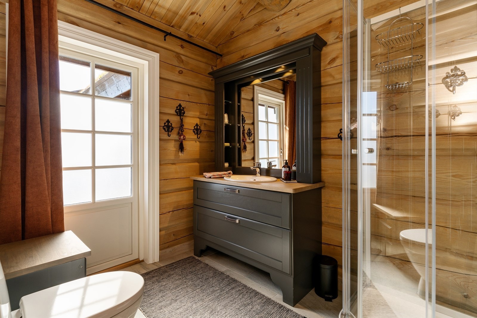 Bad med utgang til uteområde. Badet inneholder servantskap med heltre benkeplate ,servant speilskap med hyller og lys, dusjkabinett og gulvmontert toalett. Galleribilde