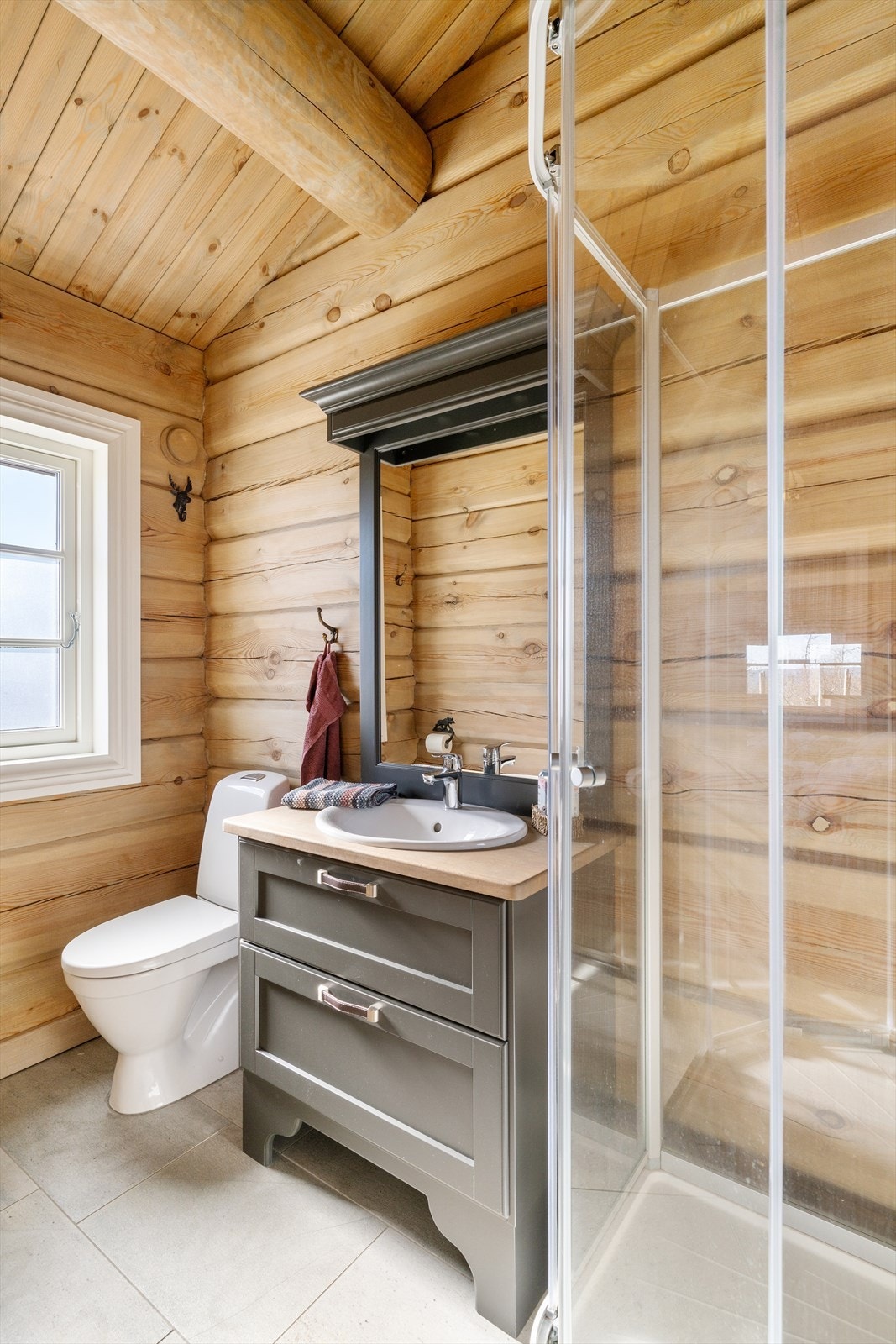 Badet inneholder servantskap med heltre benkeplate ,servant speilskap med hyller og lys, dusjkabinett og gulvmontert toalett. Galleribilde