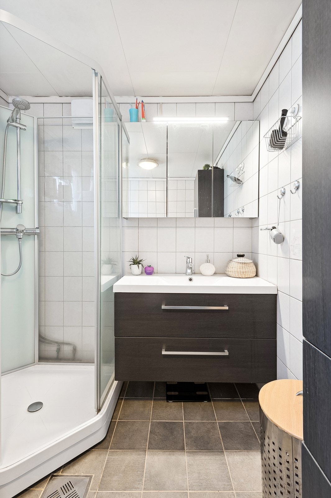 Baderomsinnredning med servant og skuffer under, speilskap med belysning over, dusjkabinett og vegghengt toalett. Galleribilde