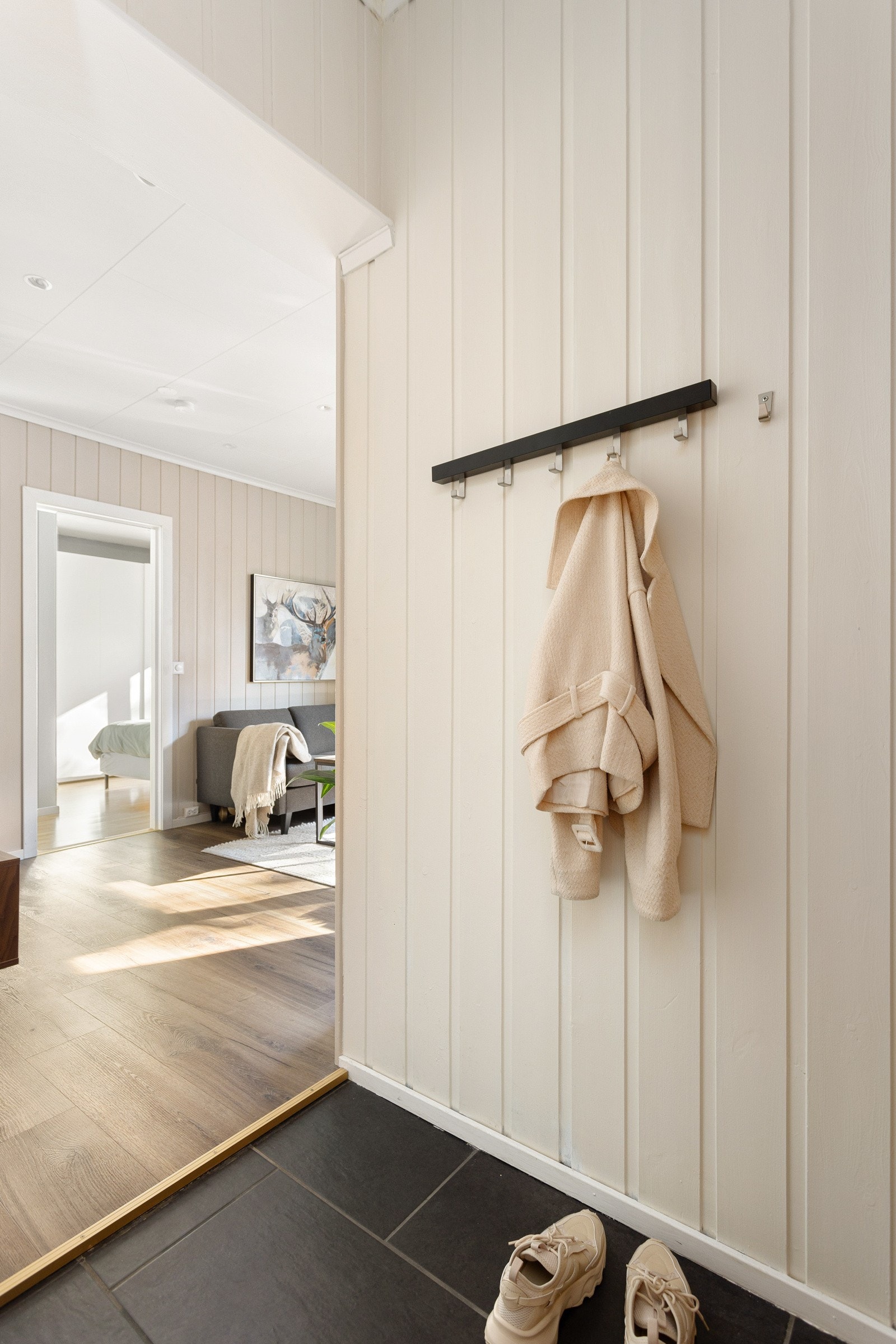 Du ønskes velkommen inn i en lys og praktisk entré med mørke fliser på gulv og lysmalt panel på veggene. Galleribilde