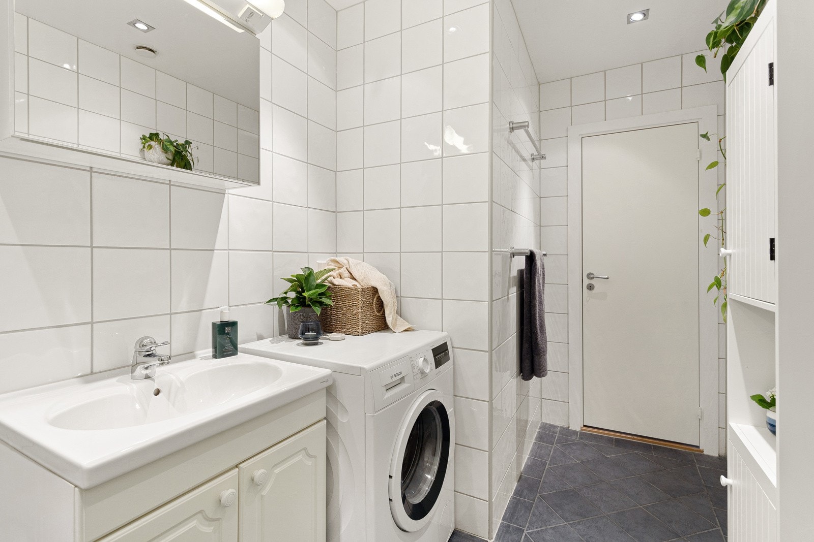 Baderommet har grå fliser på gulv med gulvvarme, hvite fliser på veggene og downlights i himlingen. Galleribilde