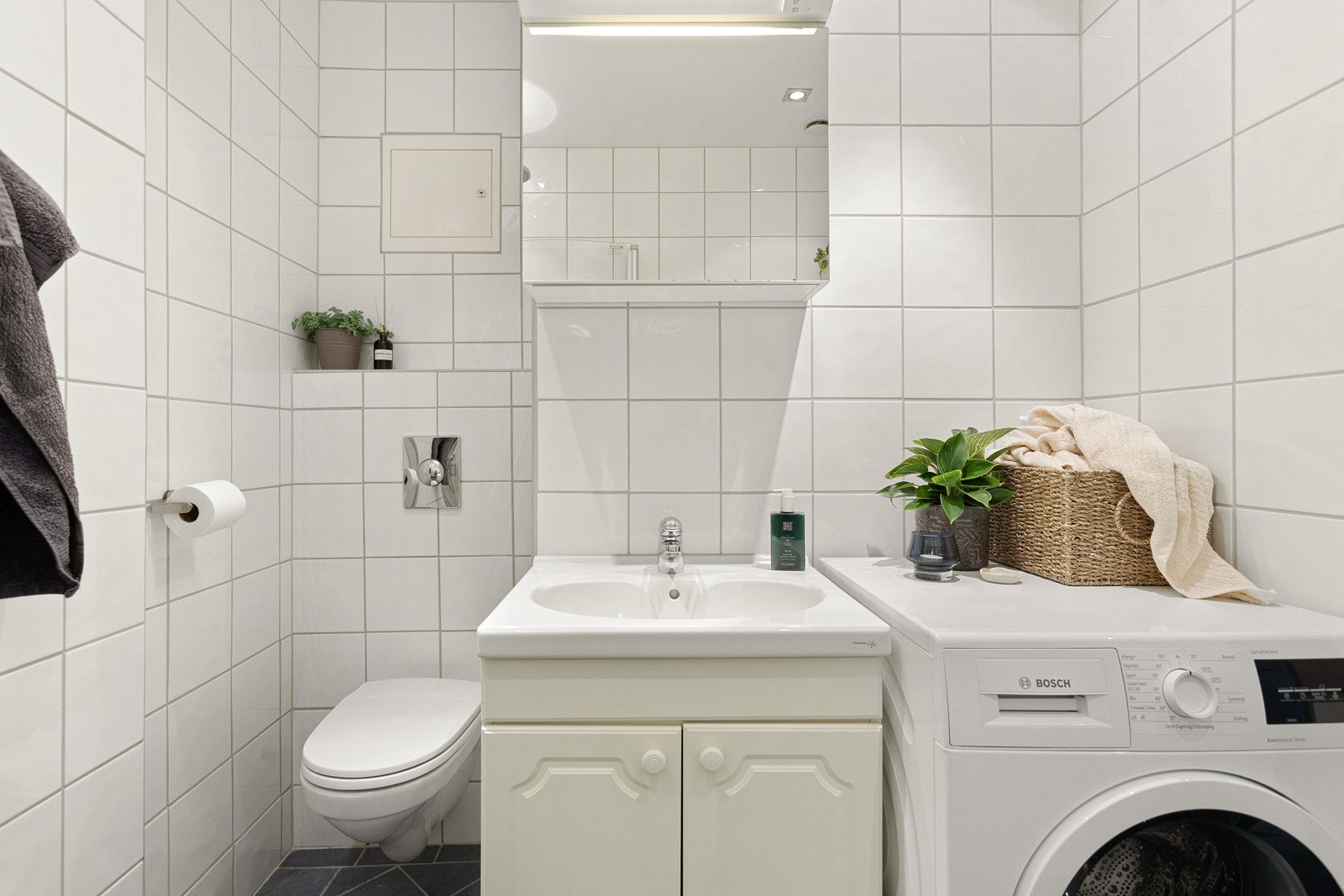 Baderomsinnredning med lyse fronter og ovenpåliggende servant, speilskap med belysning over, samt ekstra høyskap som gir god oppbevaringsplass. Galleribilde