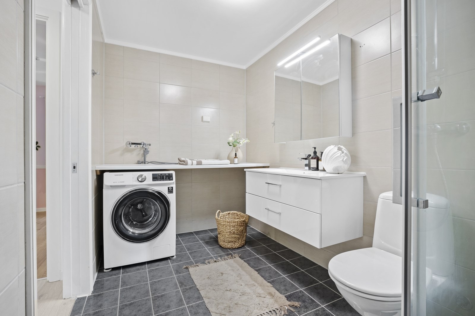 Badet er helfliset og innredet med servant, speilskap, toalett og dusj med glassvegger.
Det er også opplegg for vaskemaskin. Galleribilde