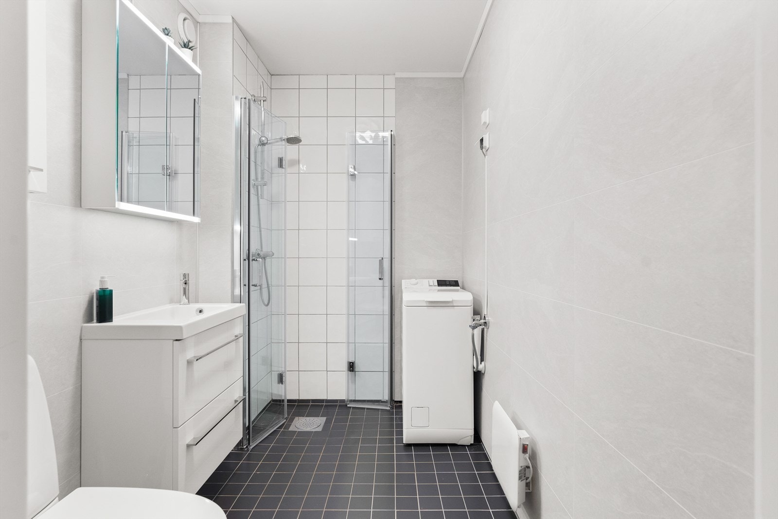 Badet har servantskap med nedfelt servant, underskuffer og 1-greps blandebatteri, samt dusjhjørne, opplegg for vaskemaskin og gulvstående toalett. Galleribilde