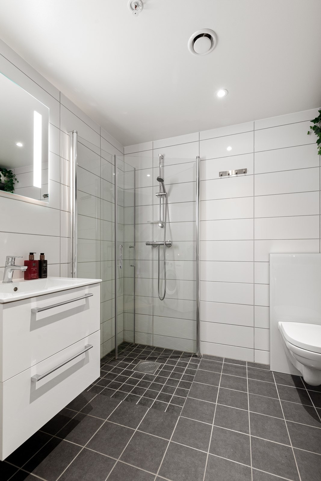 Badet inneholder heldekkende servant med underskap, speil med lys, dusjnisje med innfellbare dører og vegghengt toalett Galleribilde