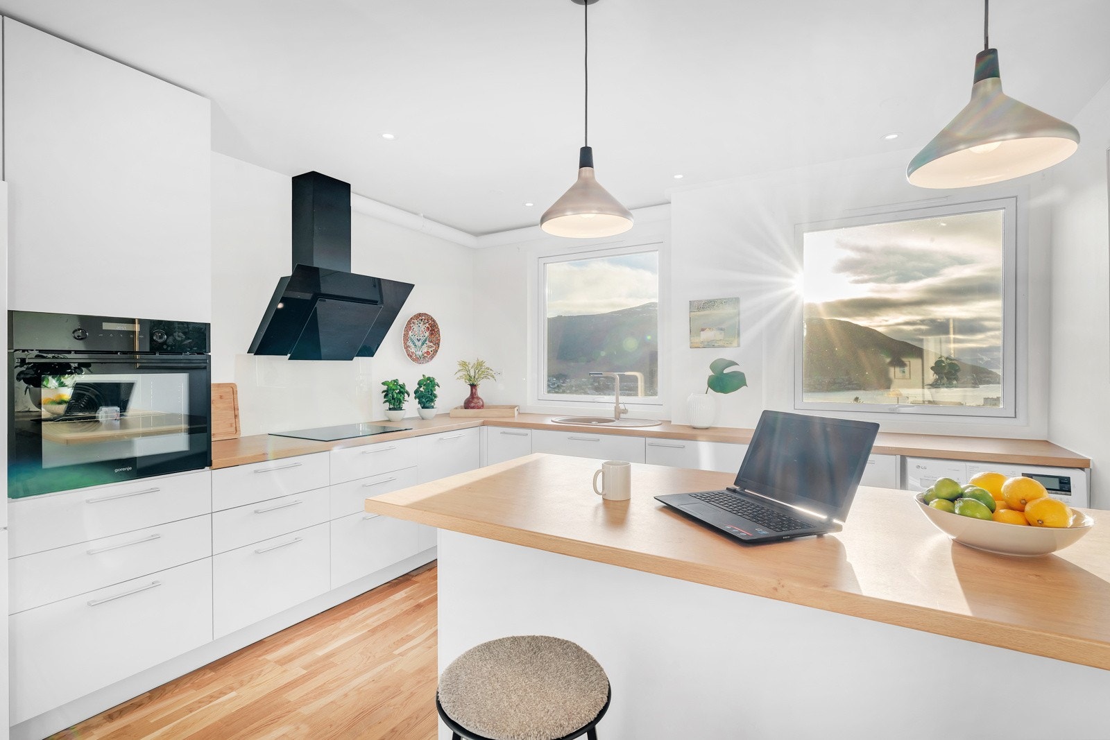 Lyst og moderne kjøkken fra 2021 innredet med glatte fronter, benkeplate i laminat og glassplate montert mellom kjøkkenbenk og overskap bak komfyr. Galleribilde