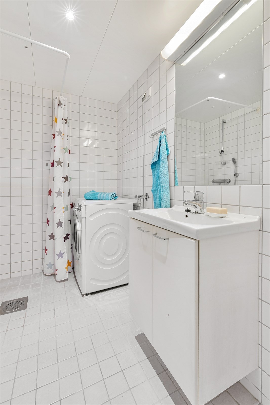 Badet er innredet med veggmontert toalett med innebygget sisterne, dusjhjørne med forheng, servant med underskap og innmurt speil med lys over. Det er opplegg for og plass til vaskemaskin. Galleribilde