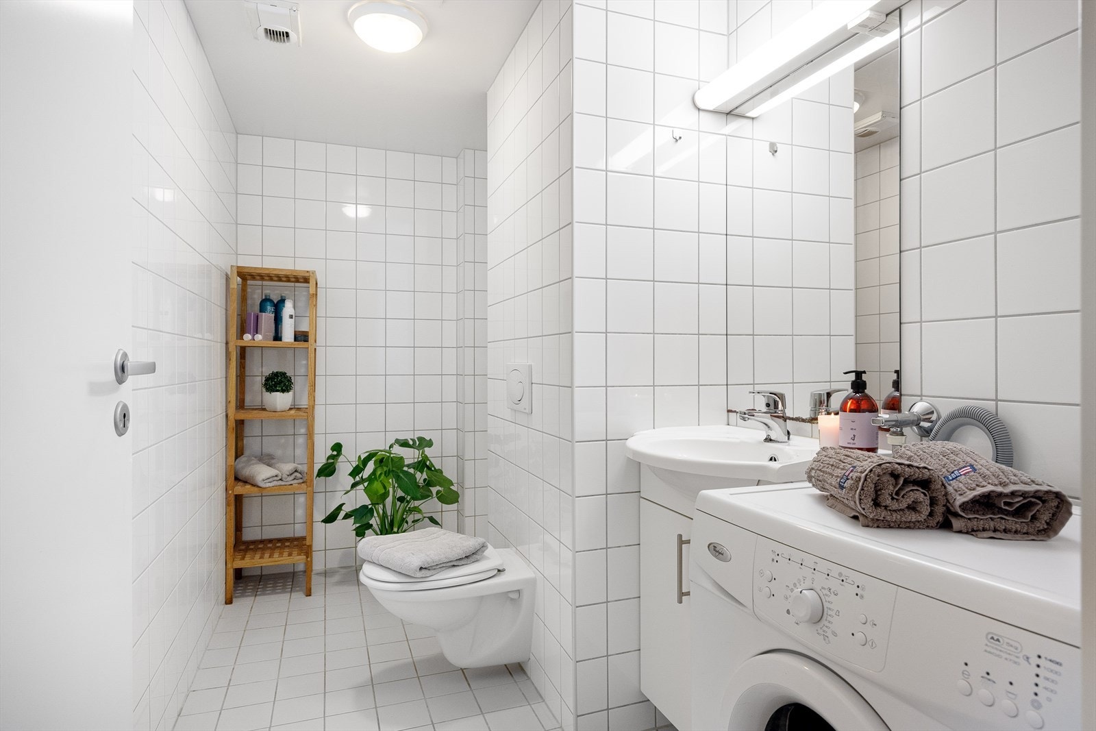 Pent flislagt baderom med gulvvarme. Badet består av servantskap med nedfelt servant, speil med belysning over, vegghengt klosett med innebygd sisterne og åpen dusjsone. Galleribilde