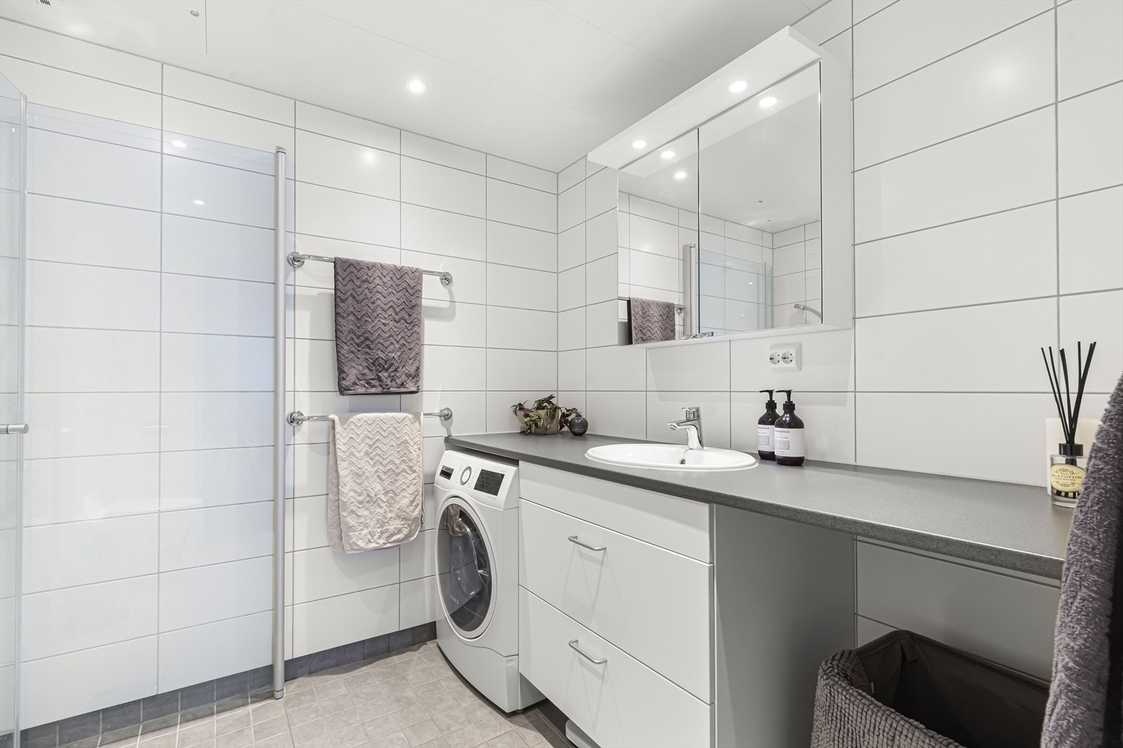 Badet består av innredning med benkeplate, servantskap med skuffer, heldekkende servant og dusjhjørne med svingbare glassdører. Galleribilde