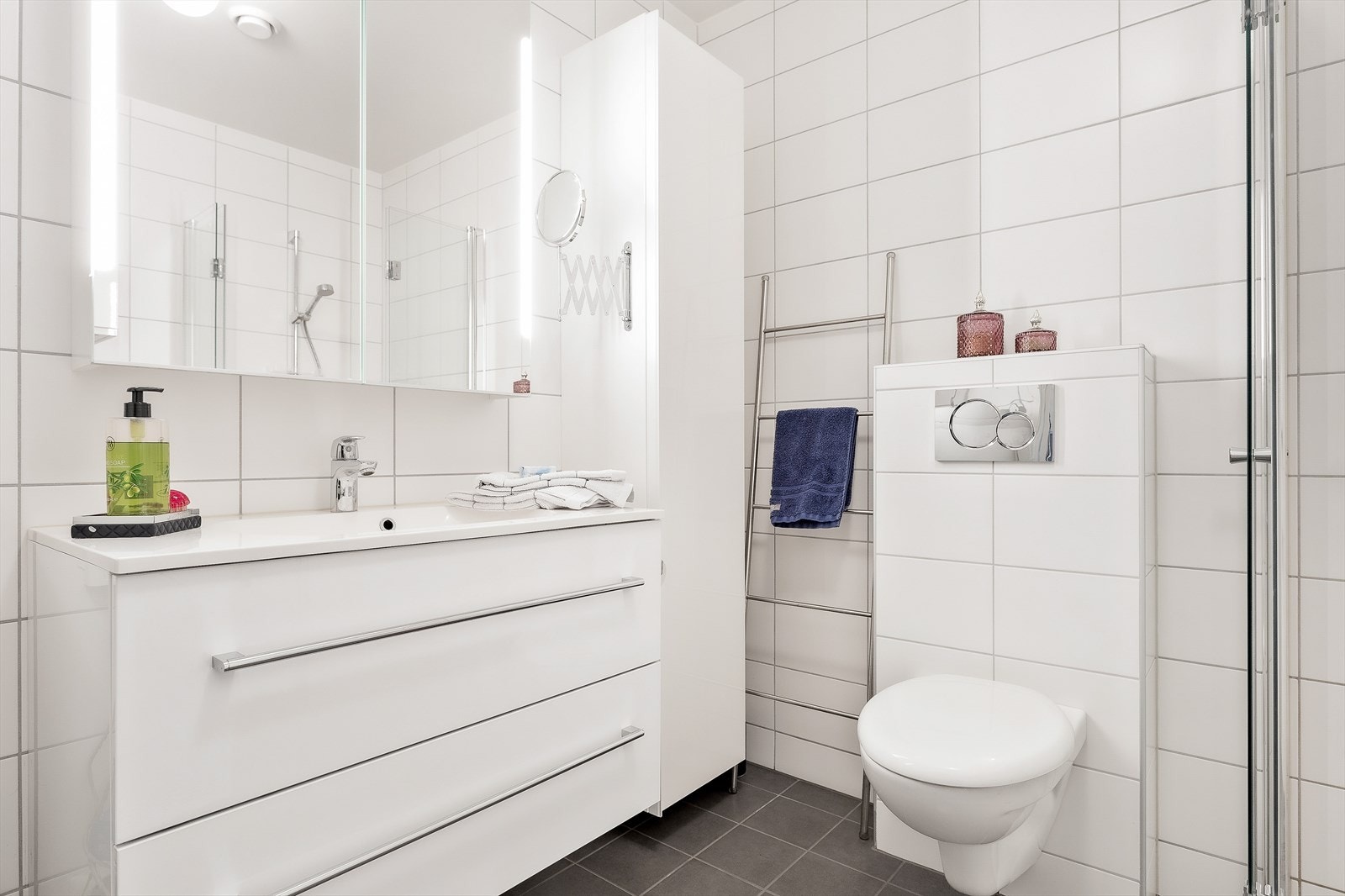 Badet er innredet med servant i baderomsinnredning, speilskap med belysning, vegghengt skap, vegghengt toalett, dusjhjørne og opplegg for vaskemaskin. Galleribilde