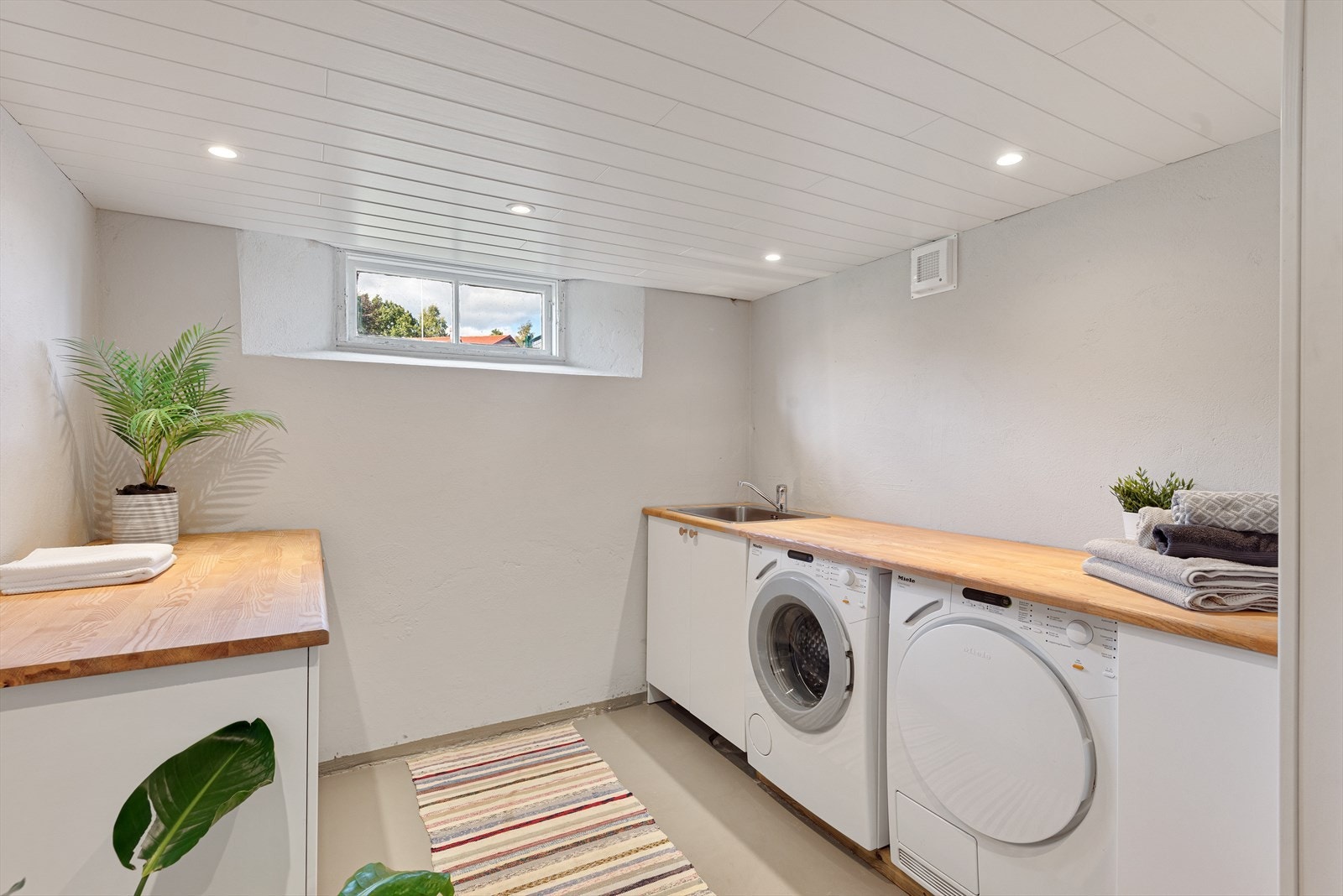 Vaskerom med malt påstøp og varmekabler på gulv og malte murvegger. MDF panel i himling med innfelte downlights. Innredet med benkeskap med nedsenket stålkum i benkeplate og opplegg for vaskemaskin og tørketrommel. Galleribilde