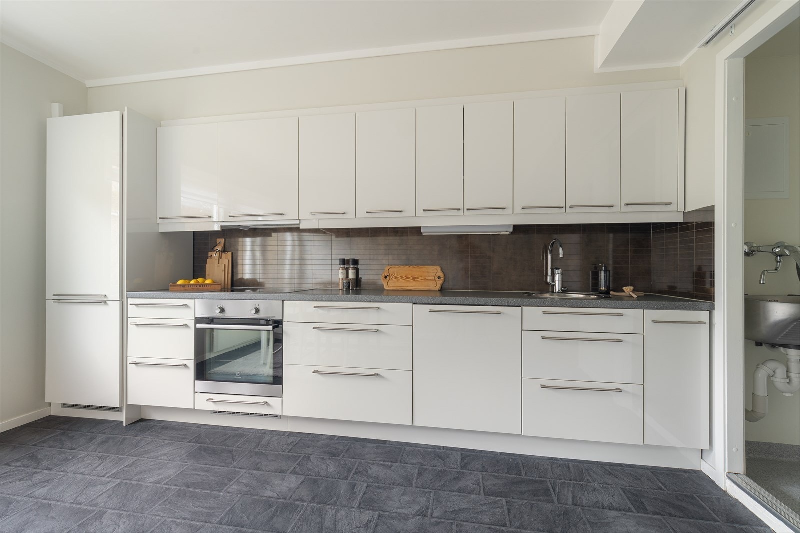 Det er kitchenboards over laminat benkeplate, med god arbeidsflate, nedfelt platetopp og nedfelt, rund oppvaskkum med ett-greps blandebatteri. Integrerte hvitevarer består av stekeovn og oppvaskmaskin. Det er avsatt plass til frittstående kjøleskap. Galleribilde