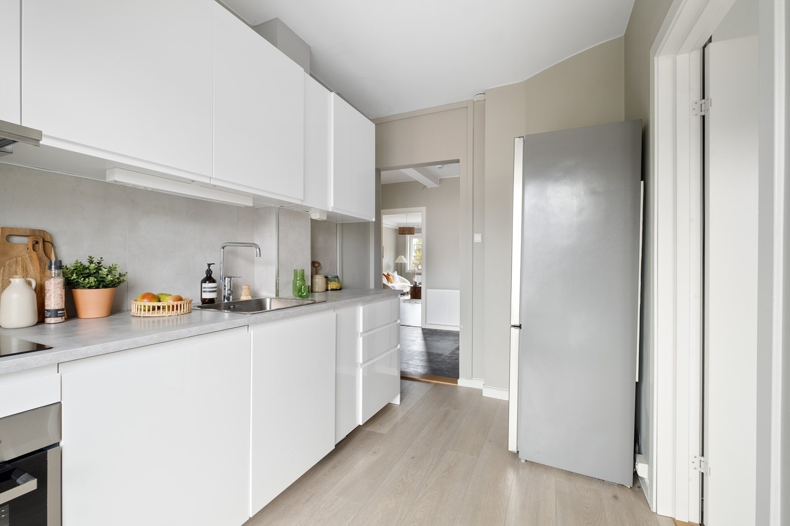Kjøkken i eget rom med hvite glatte fronter, laminat benkeplate, integrert komfyr og oppvaskmaskin, samt frittstående kjøleskap med fryser. Galleribilde