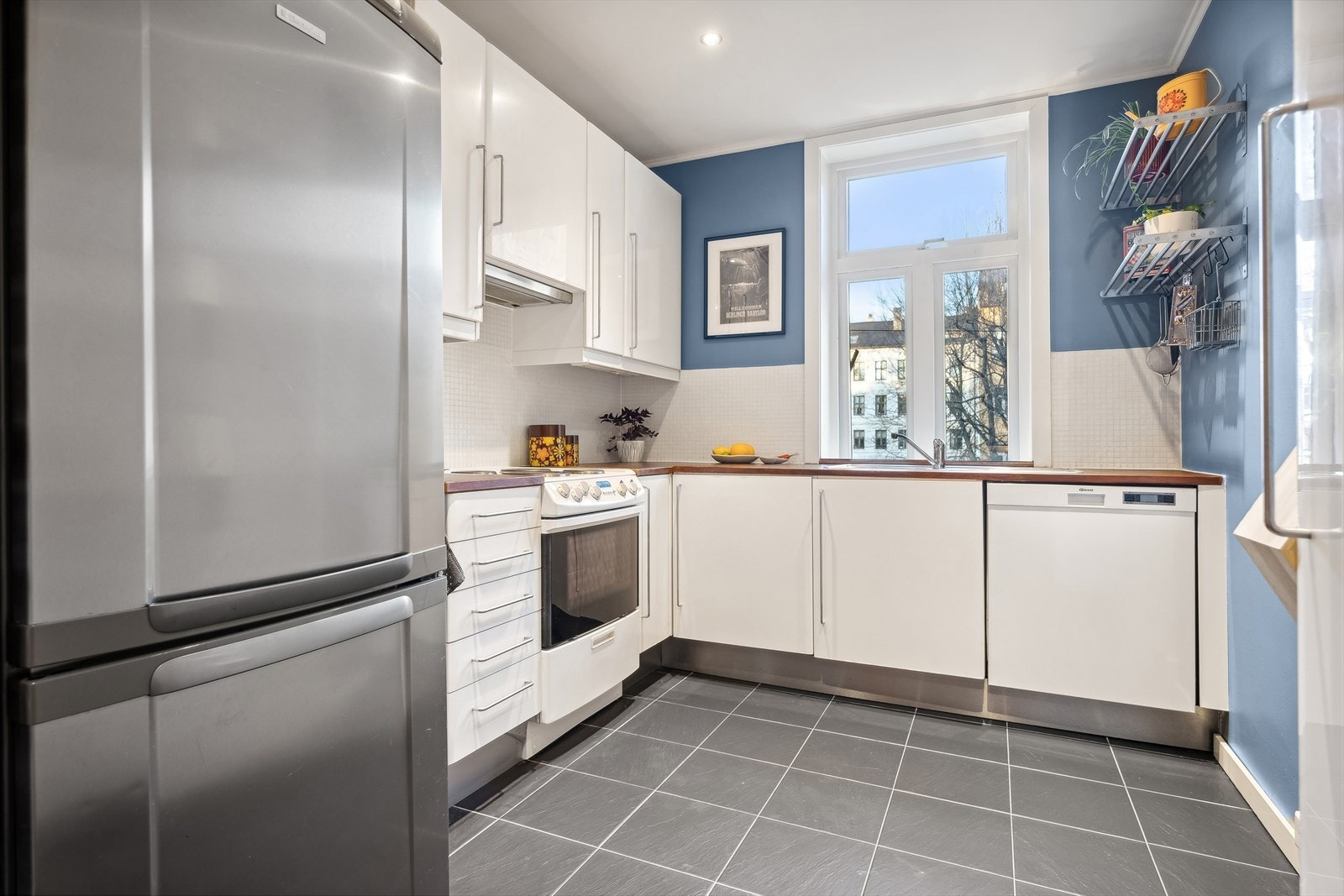 Belysning under overskap. Mosaikkfliser på vegg over benkeskap. Heltre benkeplate med nedfelt kum i rustfritt stål. Galleribilde