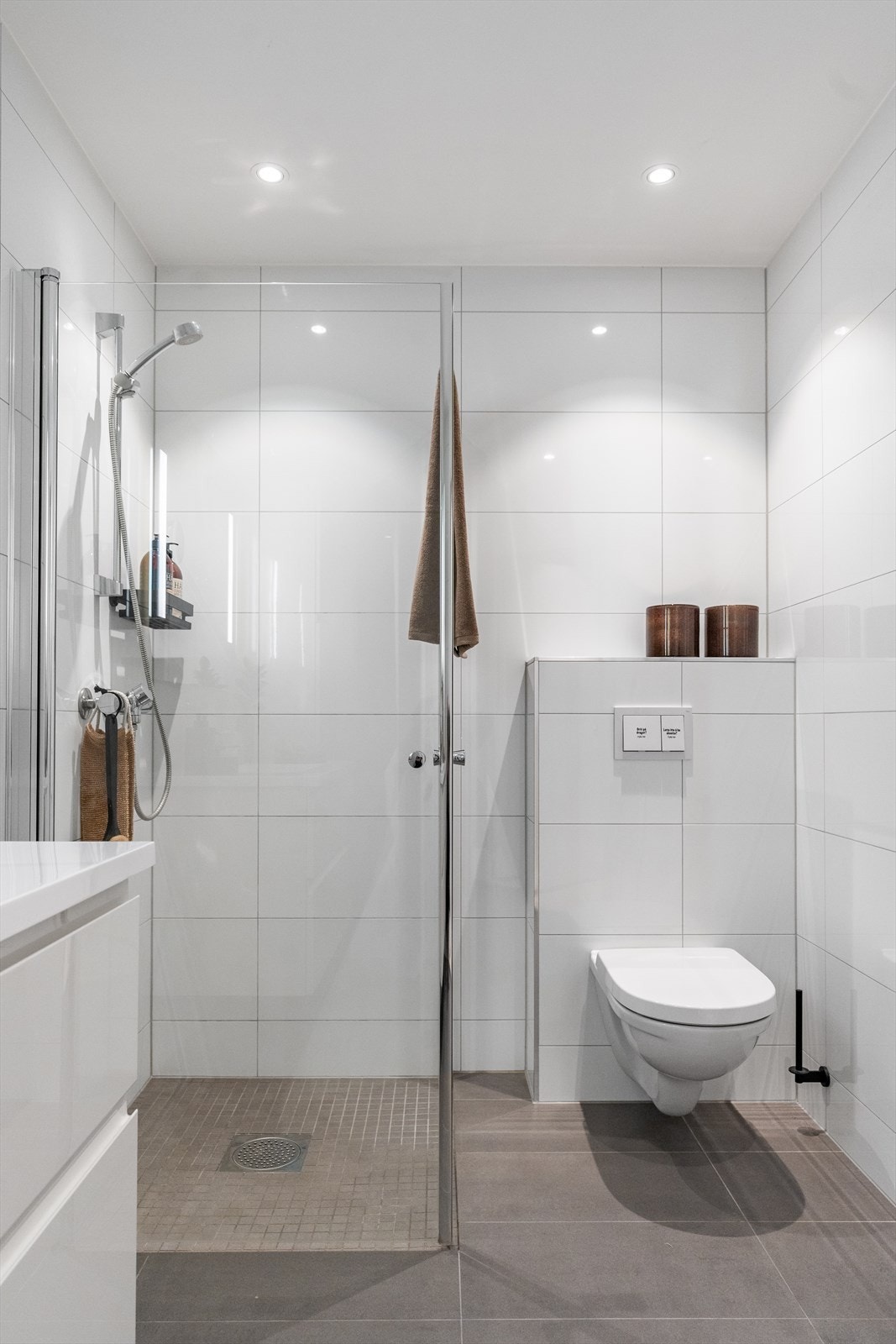 Mosaikkfliser i dusjhjørne med 2 glassdører, vegghengt toalett, hvit baderomsinnredning med stor vask og oppgradert med hvitt sideskap. Galleribilde