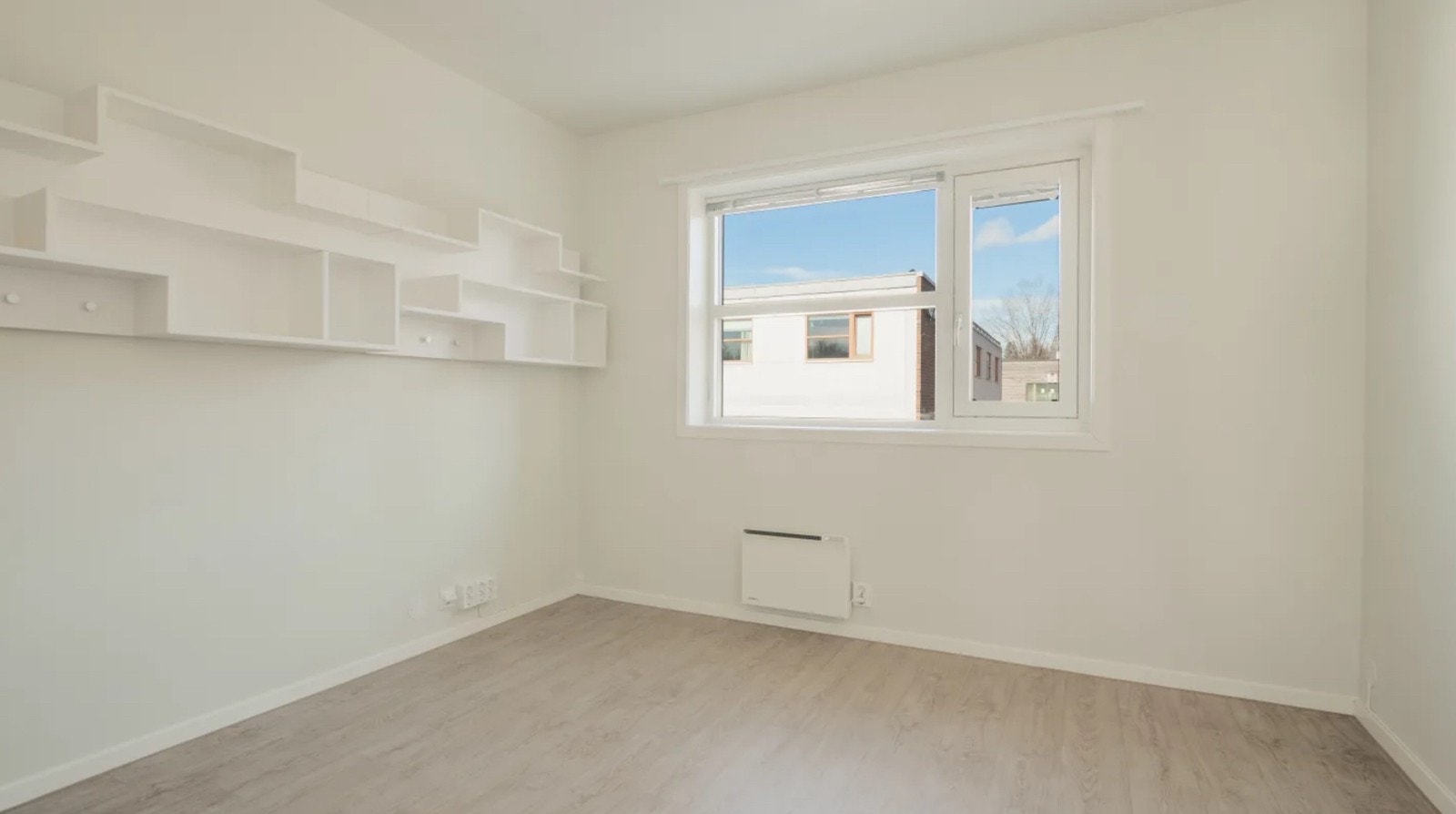 Stor hylle med knagger, panelovn, stort vindu med gardin, lite vindu som kan åpnes, mange stikkontakter under pult. Galleribilde