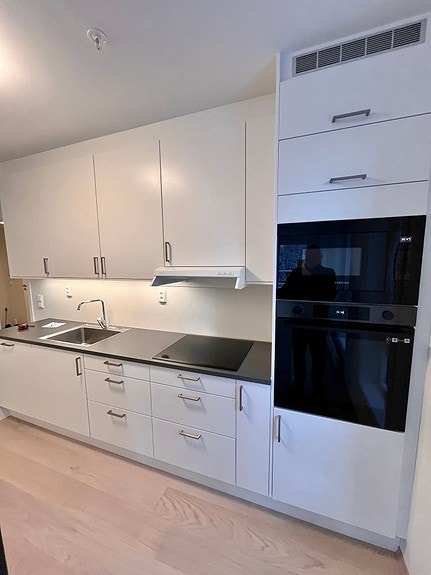 Del av kjøkken med komfyr, mikro, platetopp og oppvaskmask. Galleribilde