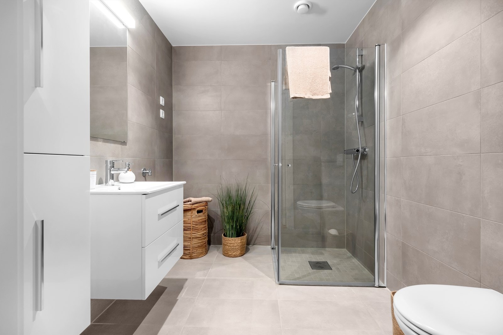 Flott baderom med vegg hengt toalett, servant med underskuffer, høyskap, dusjhjørne og opplegg til vaskemaskin Galleribilde