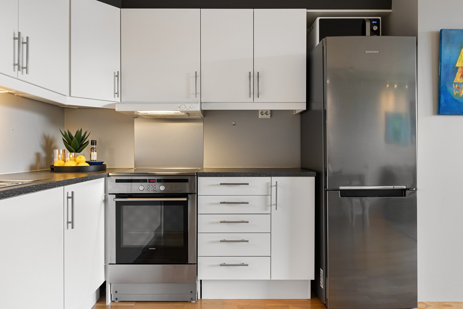 Tidløs kjøkkeninnredning med hvite glatte fronter i både over- og underskap, laminat benkeplate med oppvaskkum i stål. Galleribilde