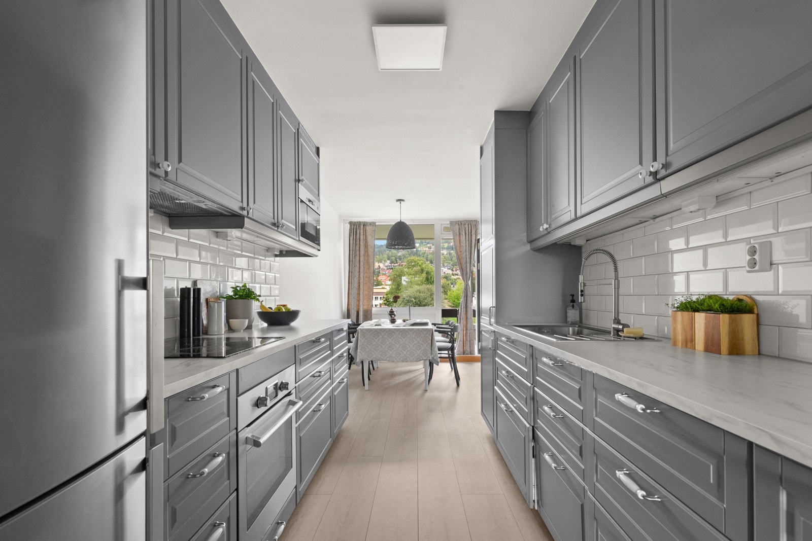 Kjøkkeninnredningen har laminert benkeplate, flislagt backsplash og profilerte fronter, samt integrerte hvitevarer, oppvaskmaskin og frittstående kjøleskap Galleribilde