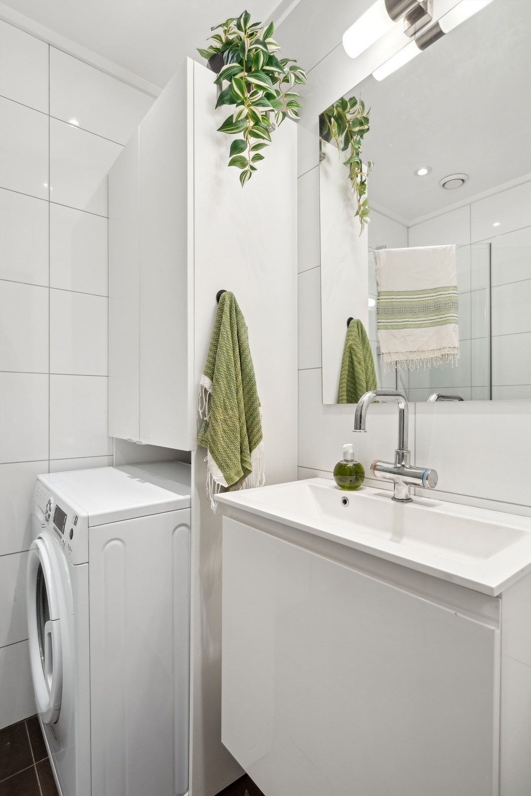 Badet består av frittstående toalett, servant med underskap, speil med overlys, veggskap, inn-/utadslående dusjdører og opplegg for vaskemaskin Galleribilde