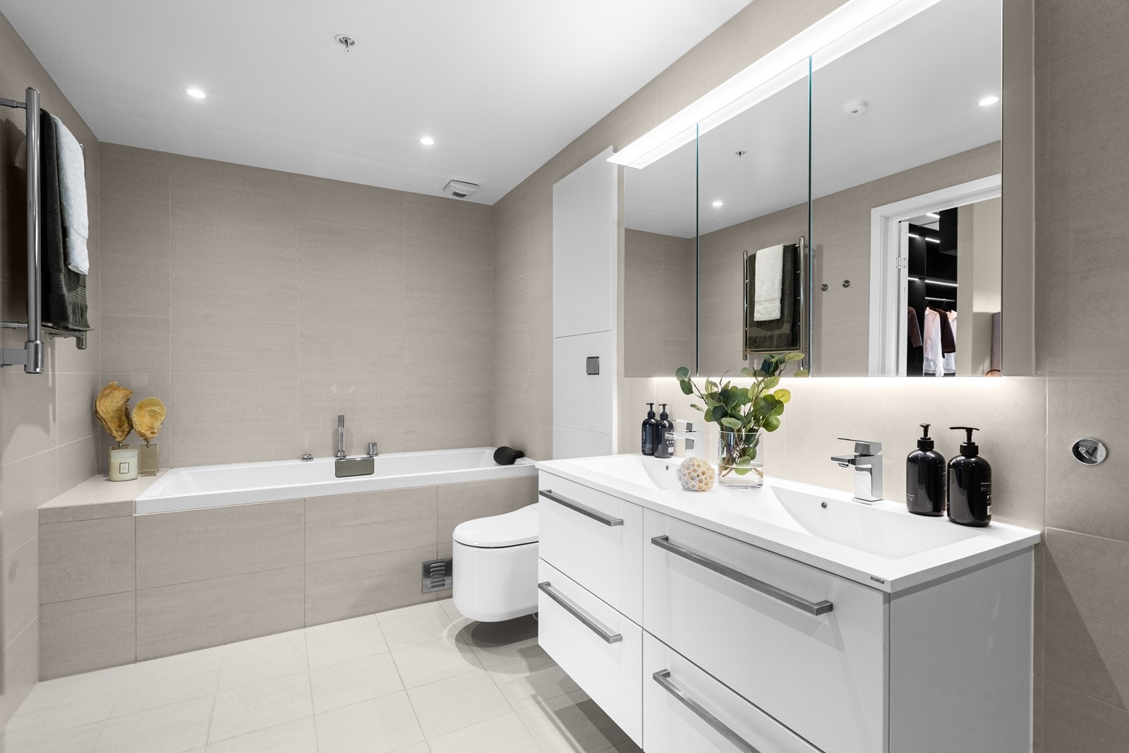 Bred servantinnredning med heldekkende dobbelservant. Videre er det et tredørs speilskap med belysning for oppbevaring Galleribilde