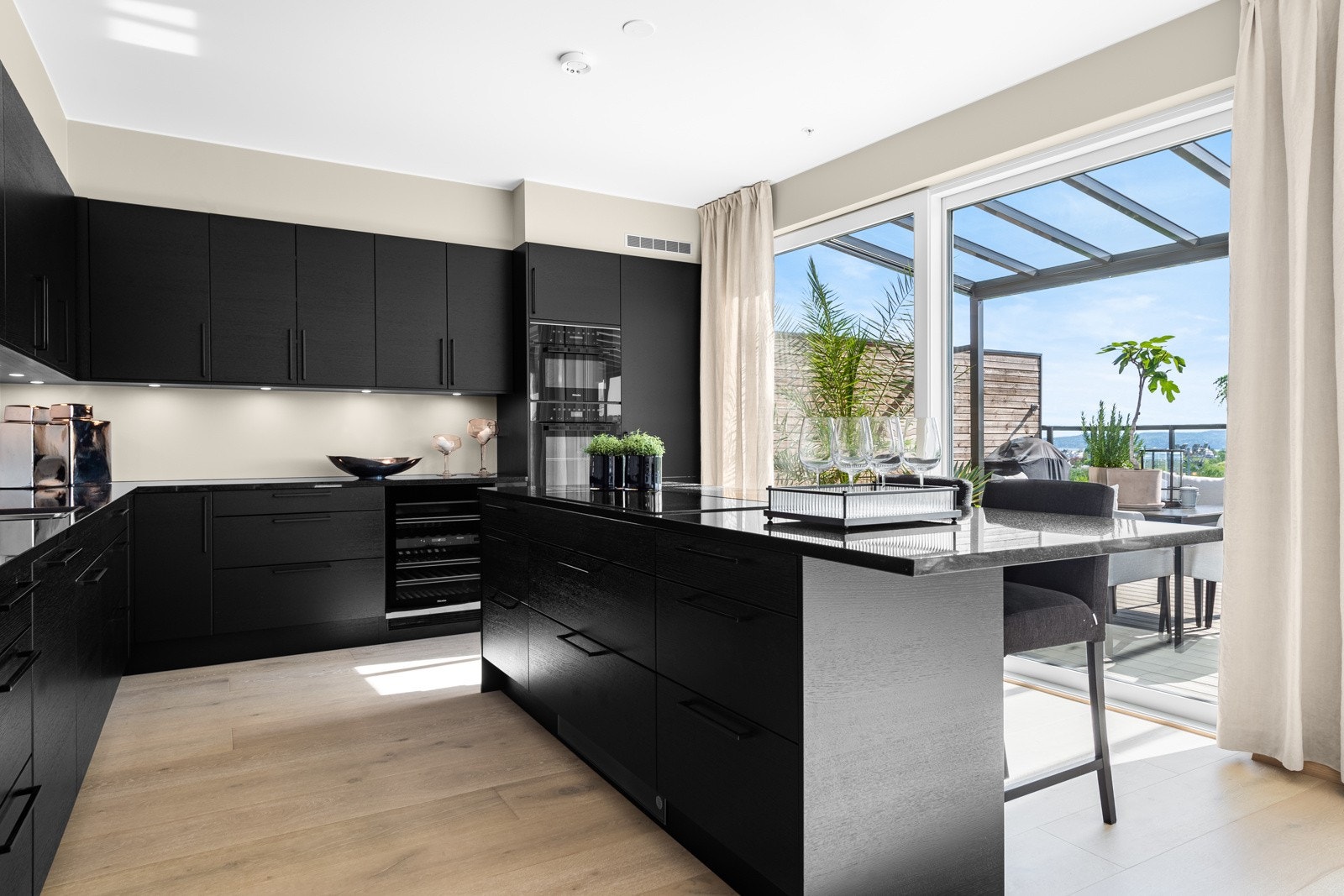 Innredningen har takoppforede skap, sorte, glatte fronter med trestruktur og en påkostet benkeplate i sort granitt med planlimt vaskekum Galleribilde