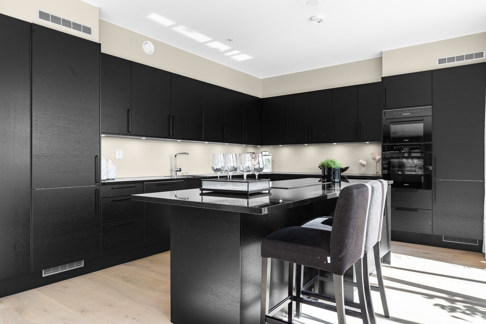 Den stilrene innredningen fra Sigdal er plassert i L-form, og har i tillegg en stor øy med barløsning, spiseplasser, dype kolonialskuffer og stikk til kjøkkenmaskiner Galleribilde