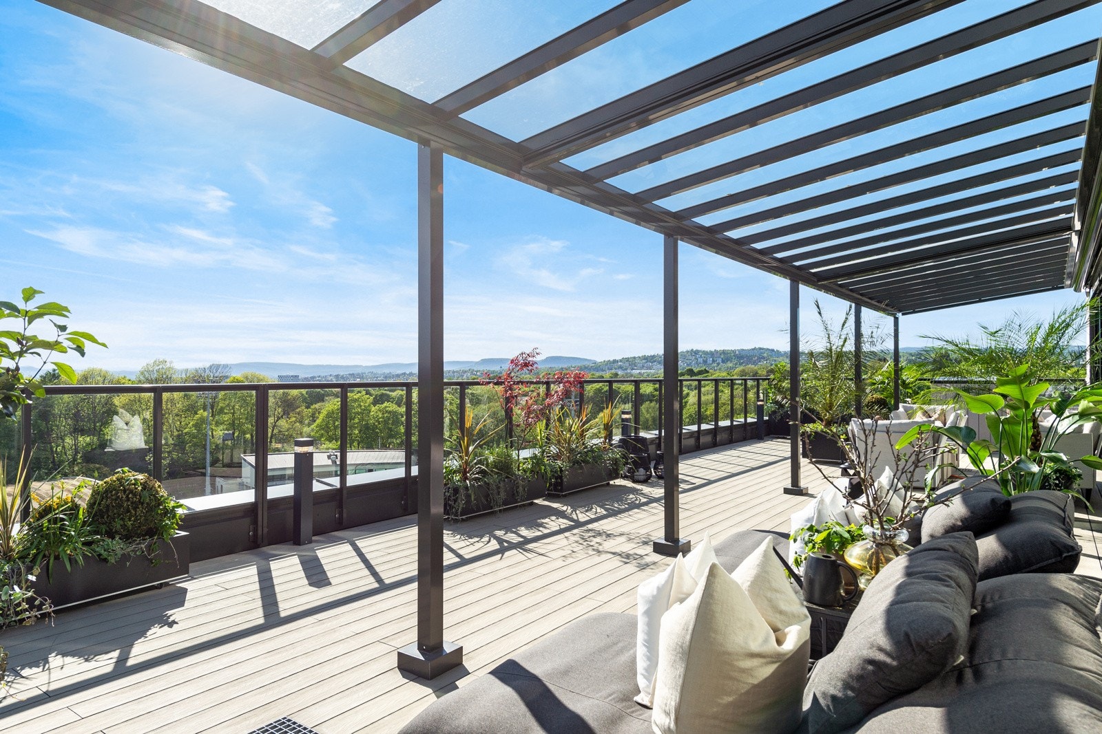 Uteplassen har dekke av vedlikeholdsfrie terrassebord, levegger på sidene, og rekkverk i glass rundt om som gir uhindret sikt Galleribilde