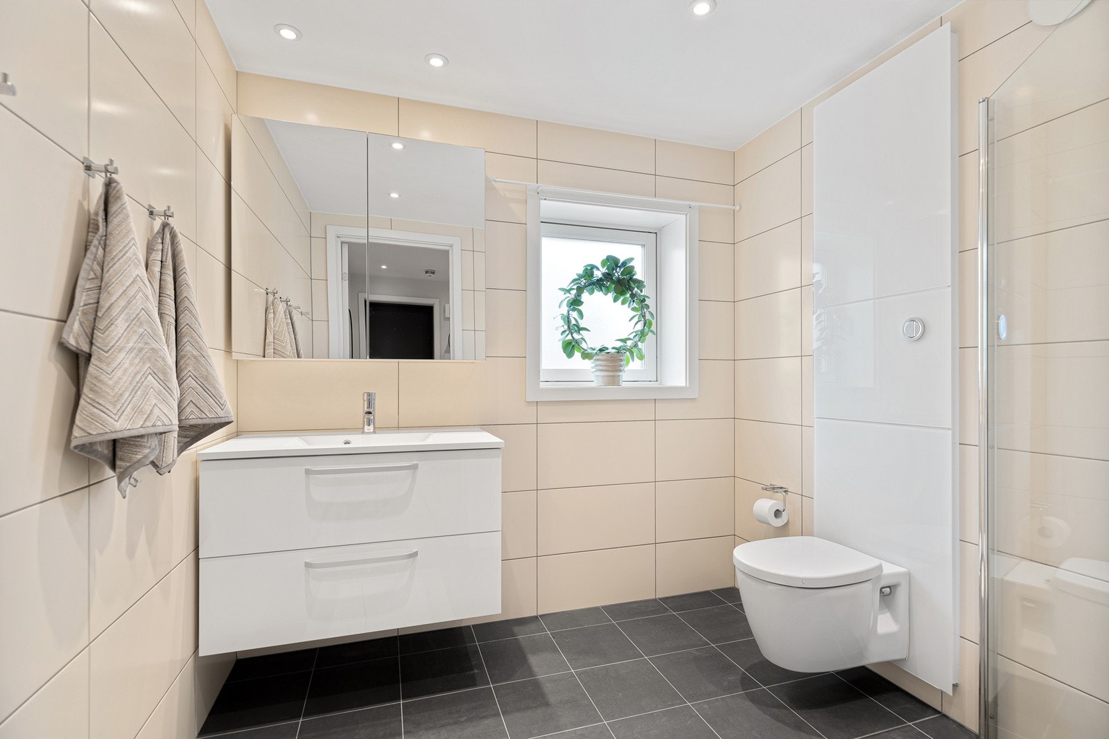 Pent flislagt bad som varmes opp med vannbåren varme i gulv. Dusjhjørne med glassdører, og servant med innredning samt speilskap. Videre er det vegghengt toalett. Galleribilde