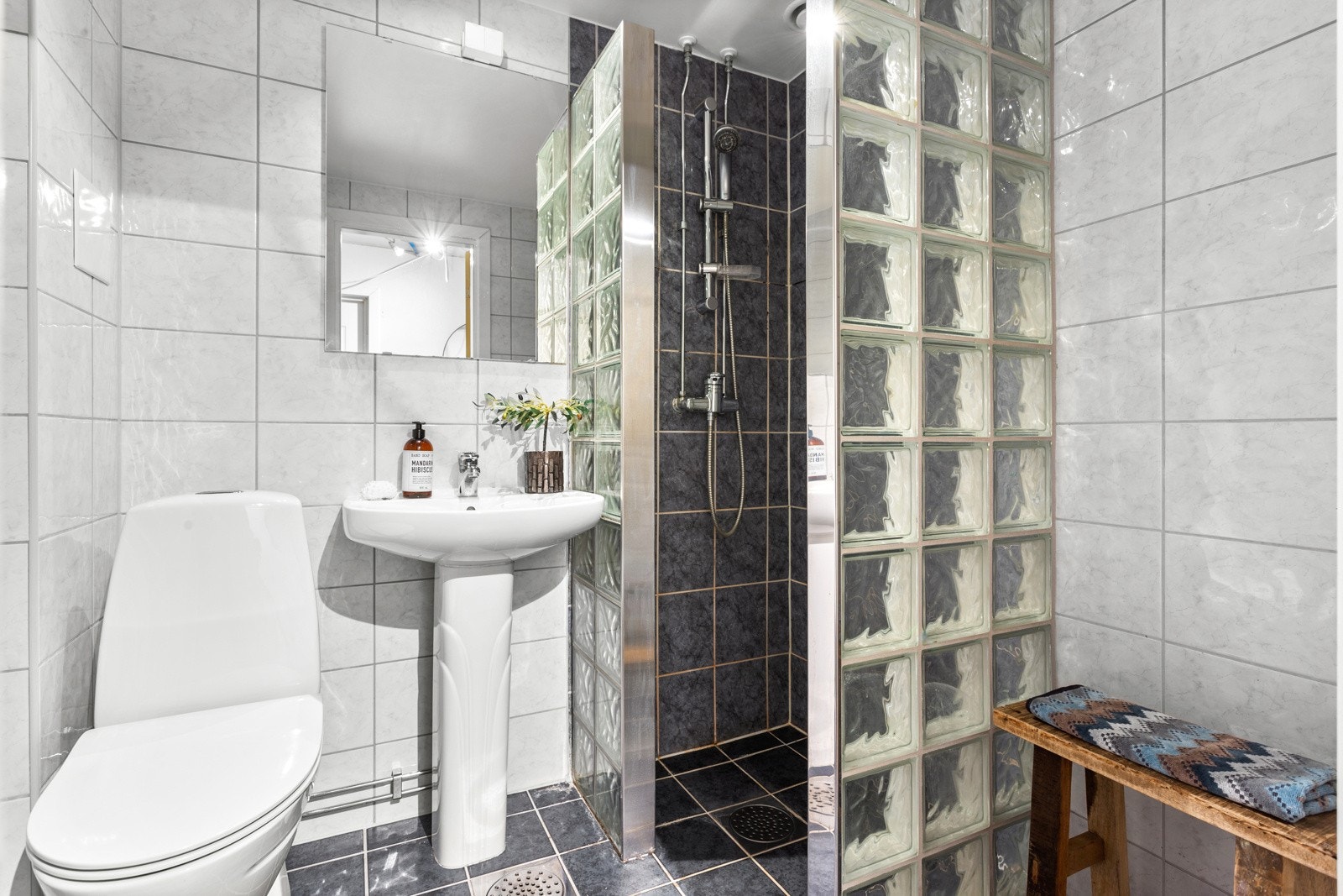 Dusjhjørnet har dusjvegger av glassbyggerstein og veggmontert dusjgarnityr. I himlingen er det downlights og det er gulvmontert toalett. Galleribilde