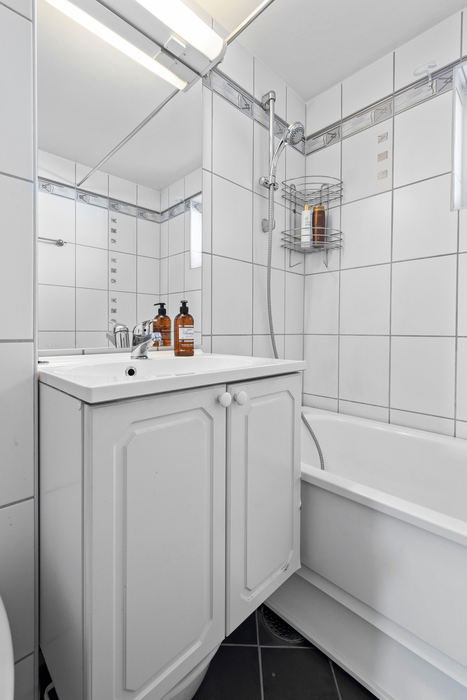 Det er vegghengt toalett og badekar med veggmontert hånddusj Galleribilde