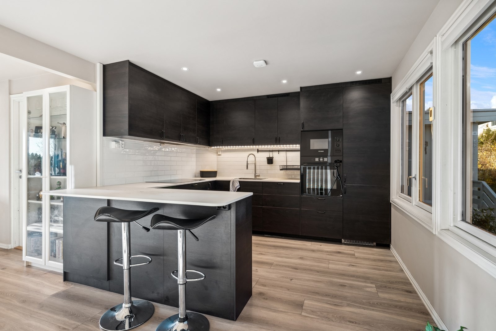 Kjøkkenet er moderne og stilrent, med en kjøkkeninnredning med brune fronter og takhøye skap som gir god oppbevaringsplass. Galleribilde