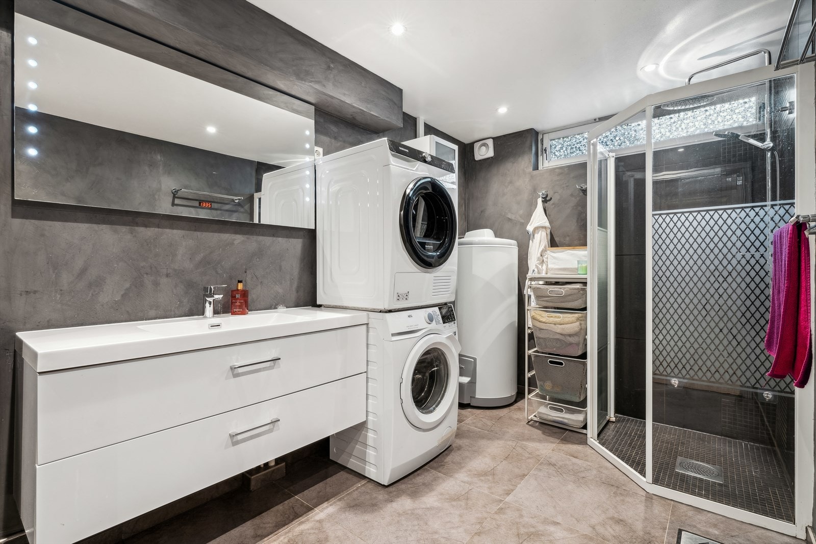 Baderommet er både praktisk og pent, utstyrt med veggmonterte dusjvegger og dusj direkte på gulvet. Det har veggmontert klosett, en servant med skuffer for god oppbevaring, og et speil med belysning. Galleribilde