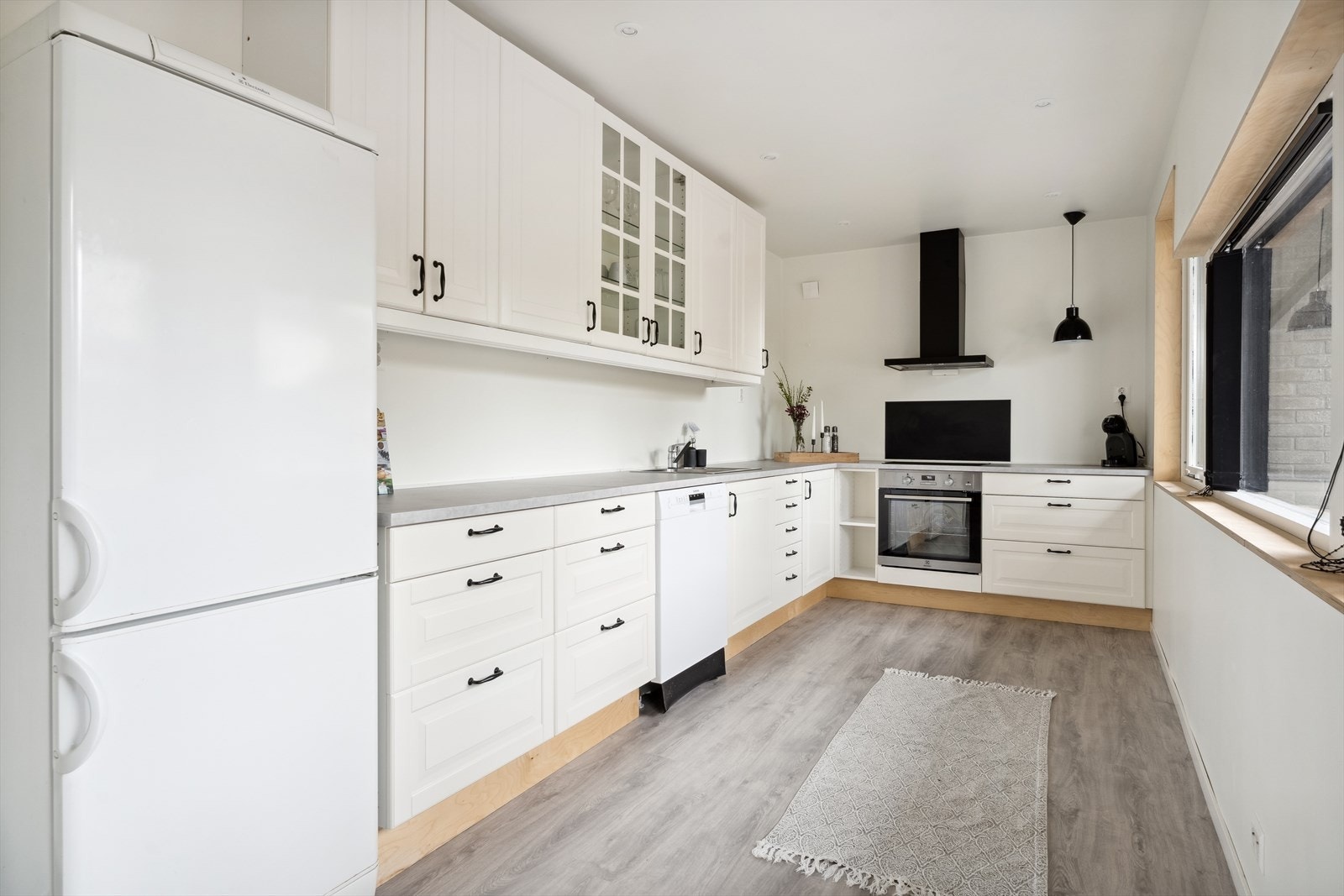 Kjøkken med kvit innreiing og vindauger ut mot terrasse og hage. Delvis itegrerte kvitevarer. Galleribilde
