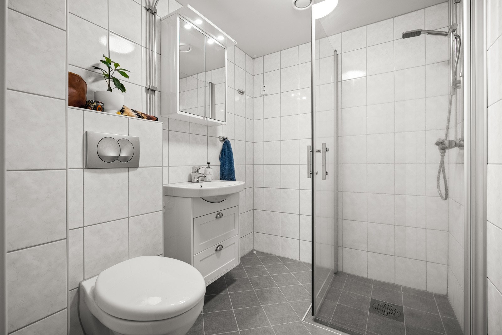 Leiligheten har et delikat bad fra 2014 med grå fliser på gulvet, lyse fliser på veggene, gulvvarme, dusjhjørne og et veggmontert toalett. Det er også plass og lagt opp til at man kan installere vaskemaskin. Galleribilde