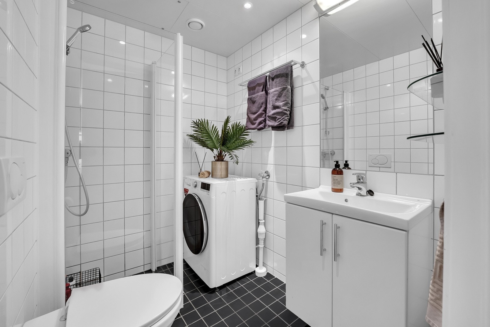 Lyst flislagt bad med gulvvarme og opplegg for vaskemaskin. Galleribilde