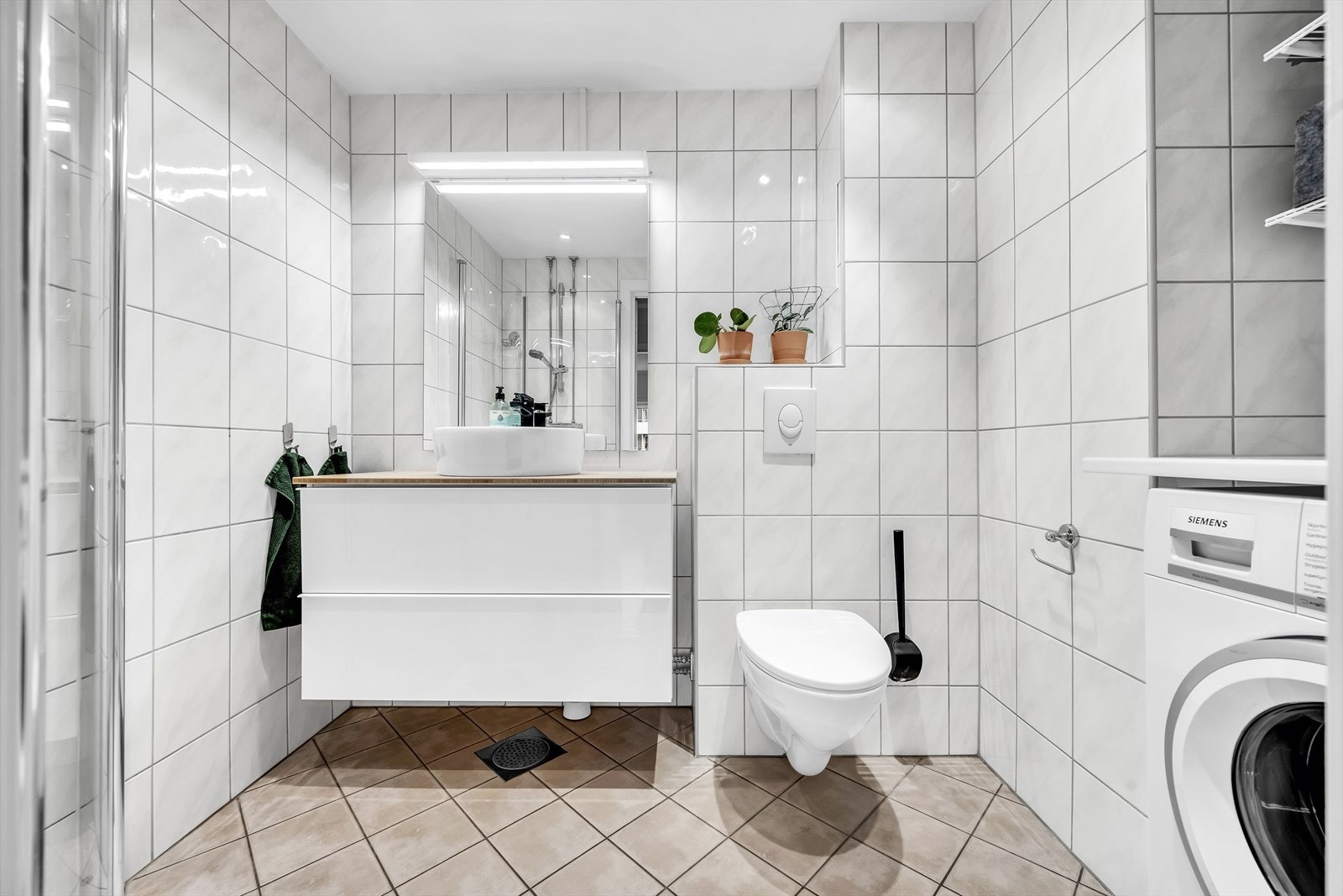 Lyst flislagt baderom med varmekabler i gulv og opplegg for vaskemaskin. Galleribilde