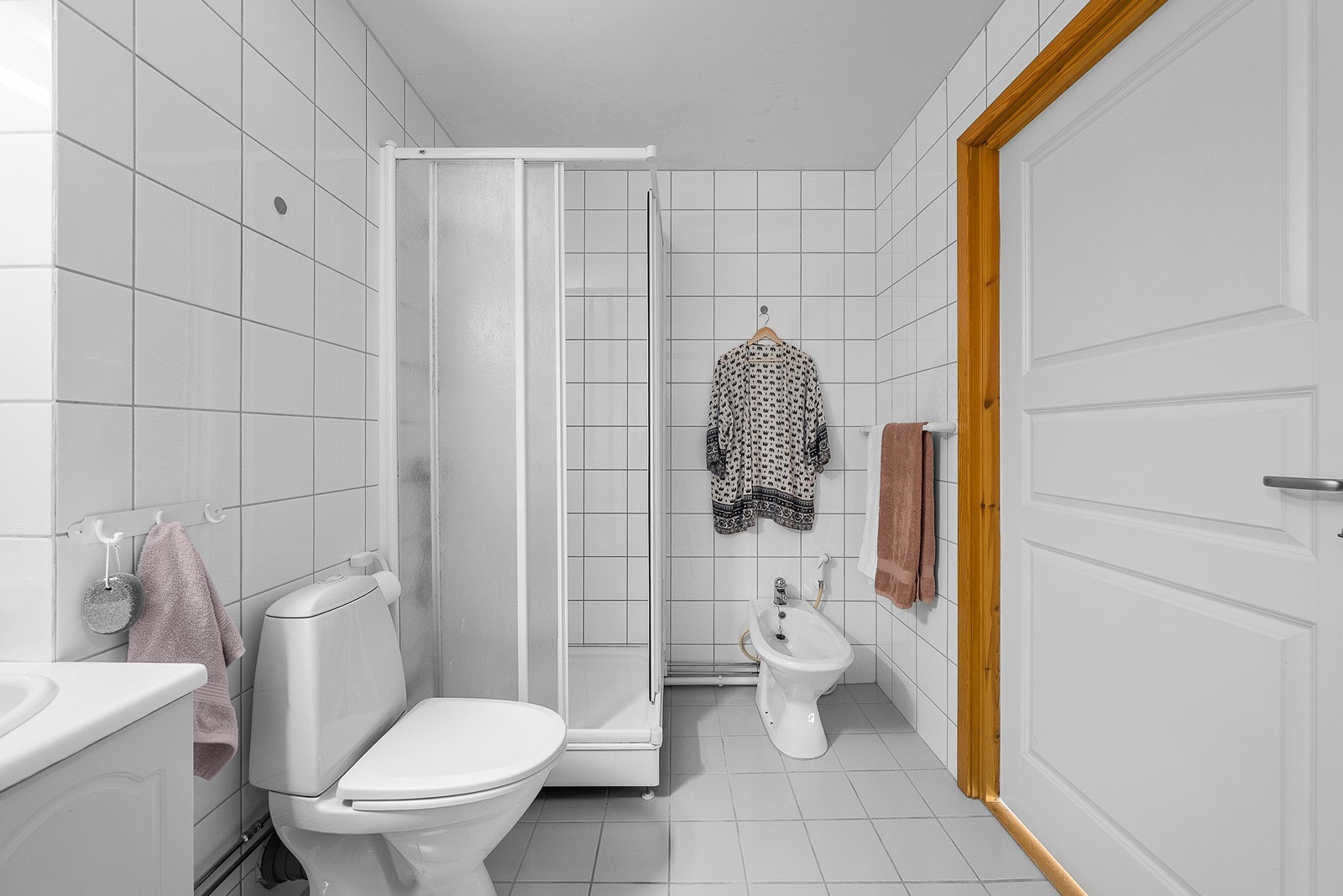 Flislagt bad med dusjkabinett, frittstående toalett, servant med underskap og bide. Galleribilde