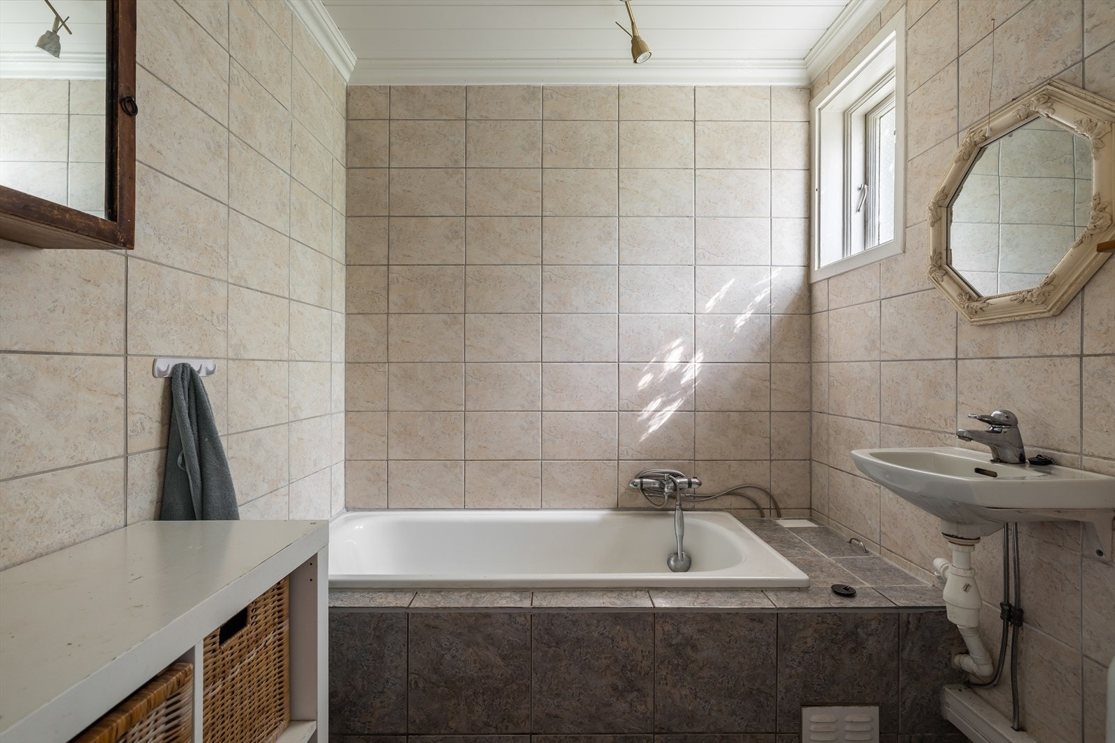 Flislagt bad som er innredet med toalett, innbygget badekar og servant på vegg. Galleribilde