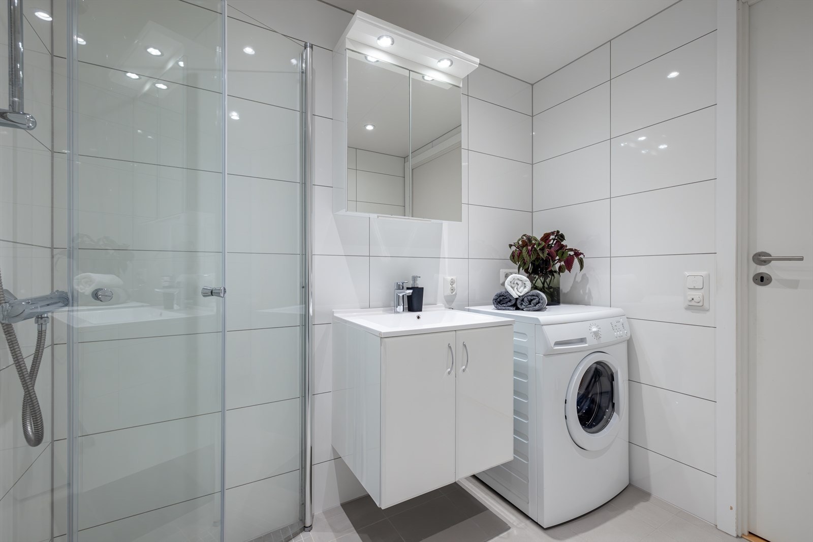 Badet er innredet med nedfelt servant, veggmontert toalett, dusjvegger/hjørne og opplegg for vaskemaskin. Galleribilde