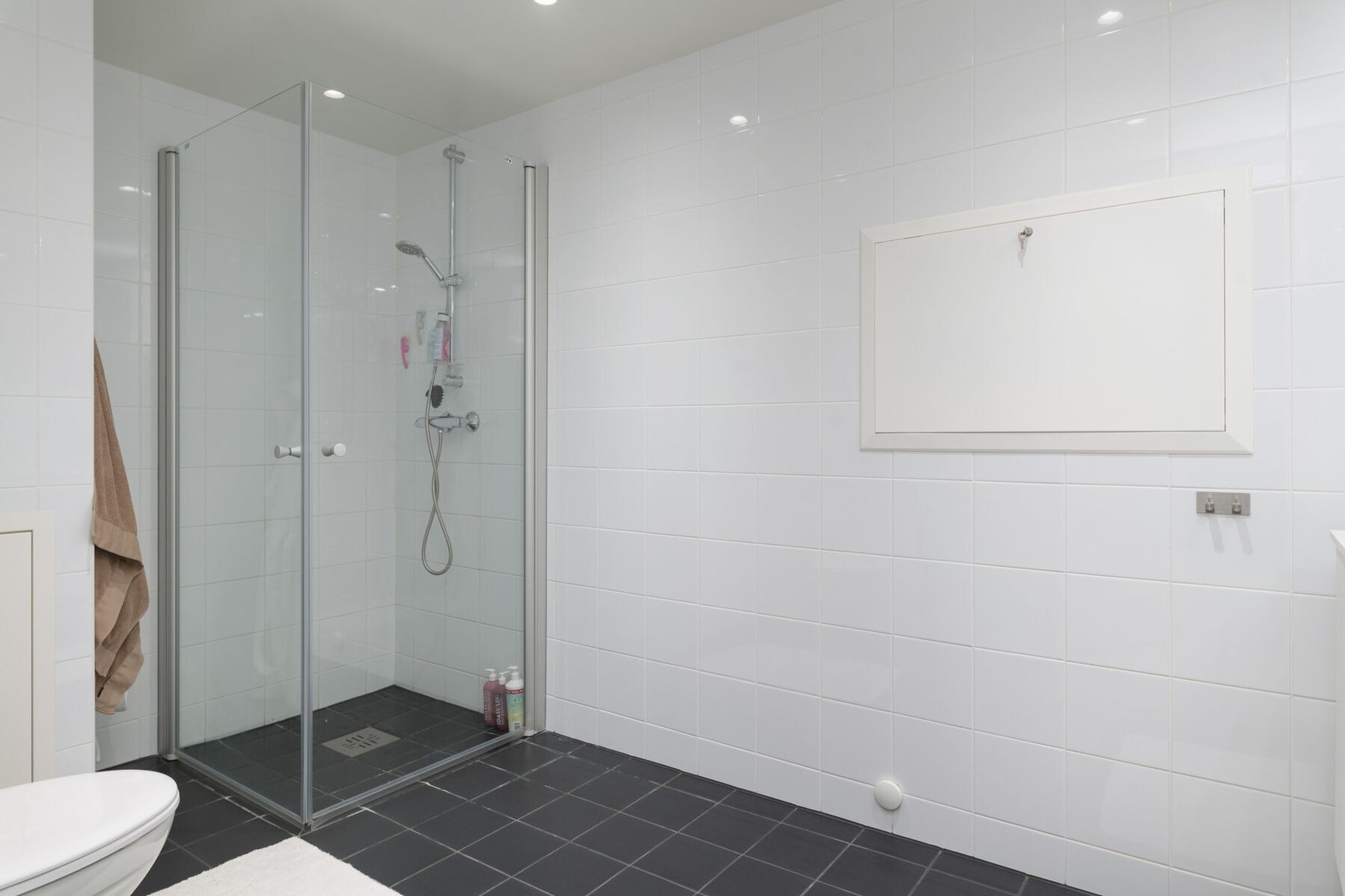 Badet har dusjhjørne, veggmontert toalett og lys baderomsinnredning med servant og speilskap, Galleribilde