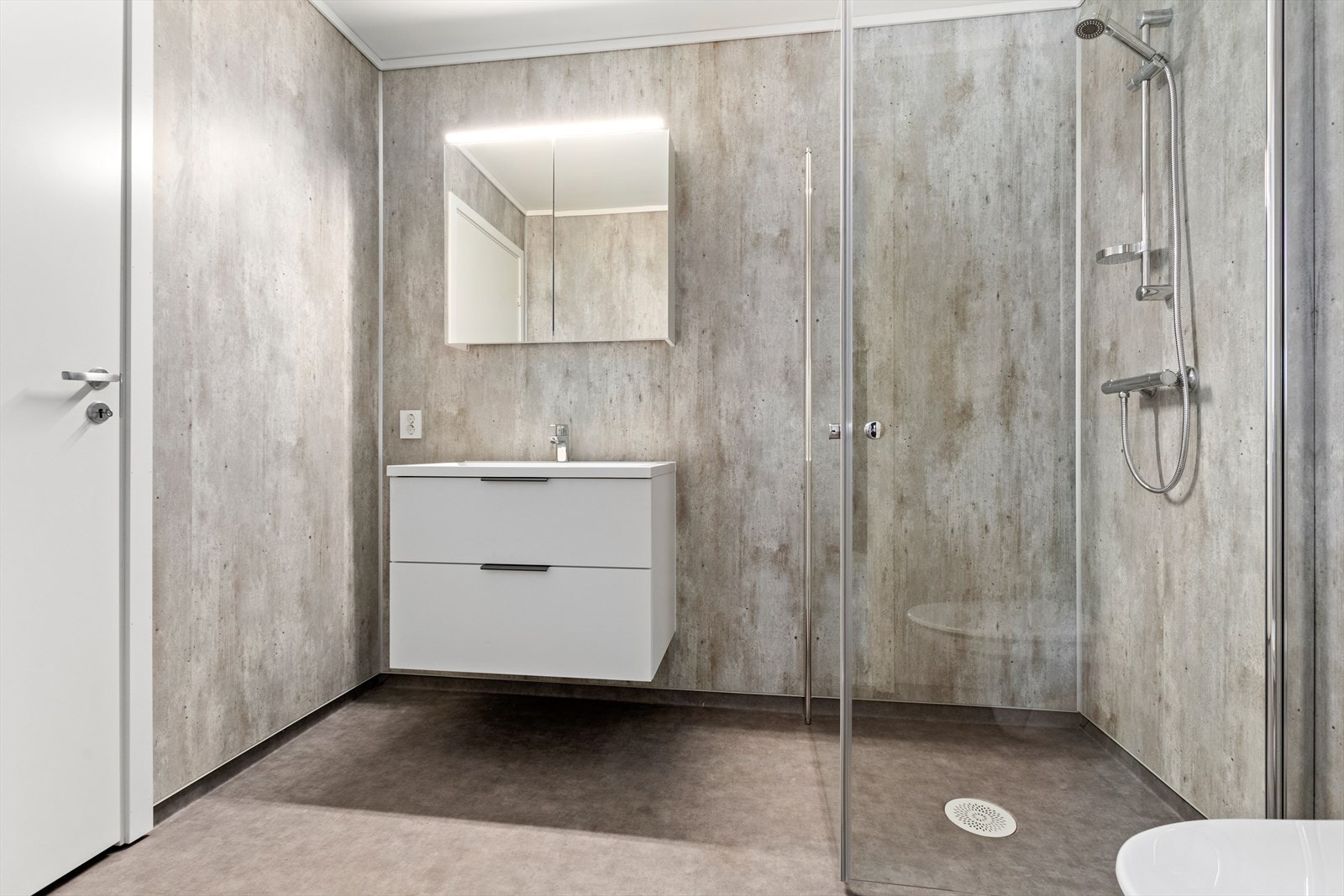 Vidare er badet utstyrt med baderomsmøbel, speilskap, dusjhjørne og vegghengt toalett. Galleribilde